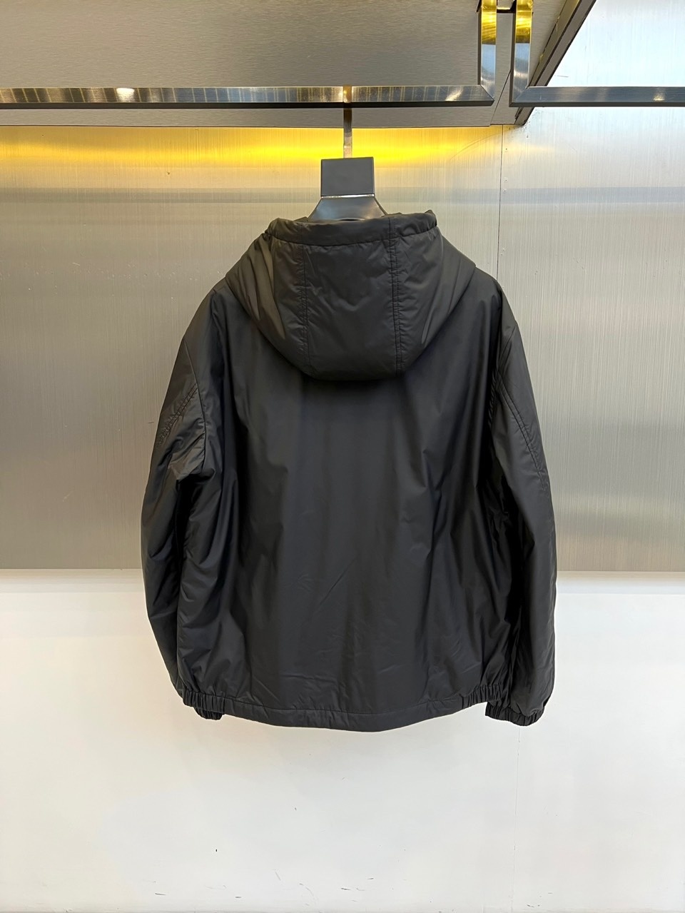 Mon蒙口、2025秋冬新品 男士连帽棉服夹克外套。这款黑色夹克采用立领连帽设计,帽檐与前襟配备银色金属