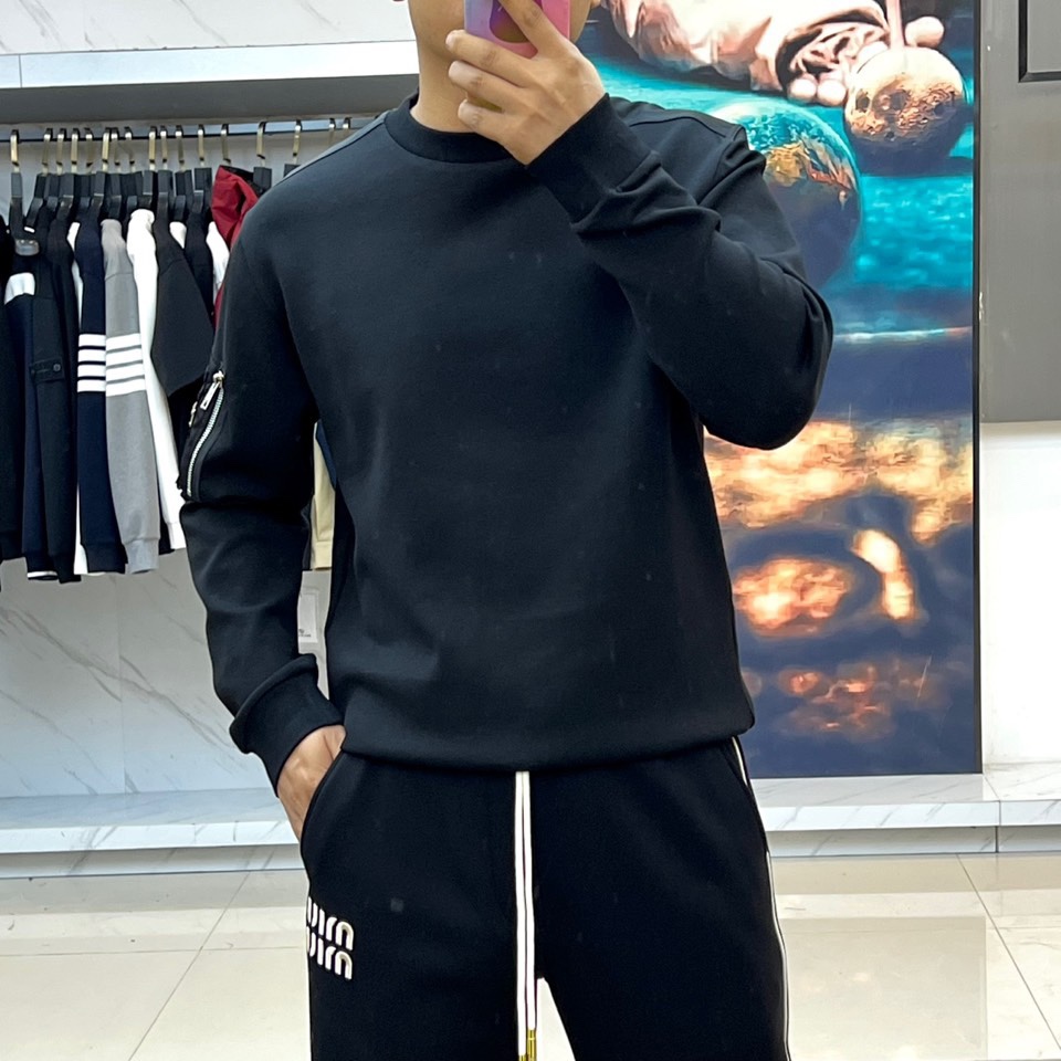 Prad普拉、2025秋冬新品 P家极简功能卫衣。这款黑色圆领卫衣采用简约立体剪裁，左臂处的银色拉链口袋