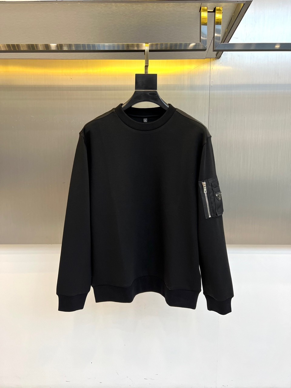 Prad普拉、2025秋冬新品 P家极简功能卫衣。这款黑色圆领卫衣采用简约立体剪裁，左臂处的银色拉链口袋