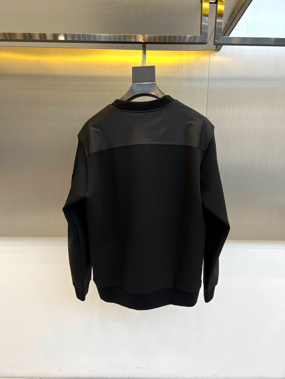 Prad普拉、2025秋冬新品 P家极简功能卫衣。这款黑色圆领卫衣采用简约立体剪裁，左臂处的银色拉链口袋