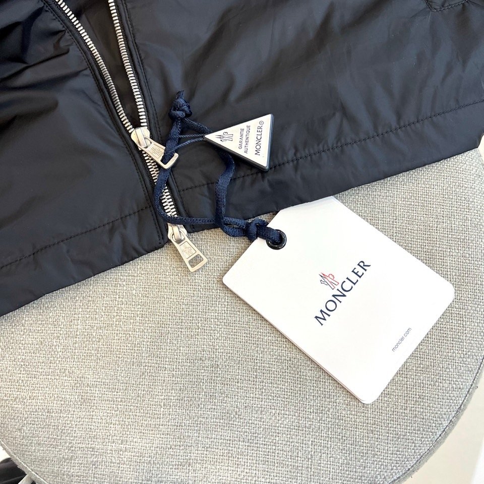 Mon蒙口、25s秋冬新品连帽夹克。冷调纯白如阿尔卑斯新雪，金属背景的钨丝灯光为衣身镀上暖金。拉开拉链乍