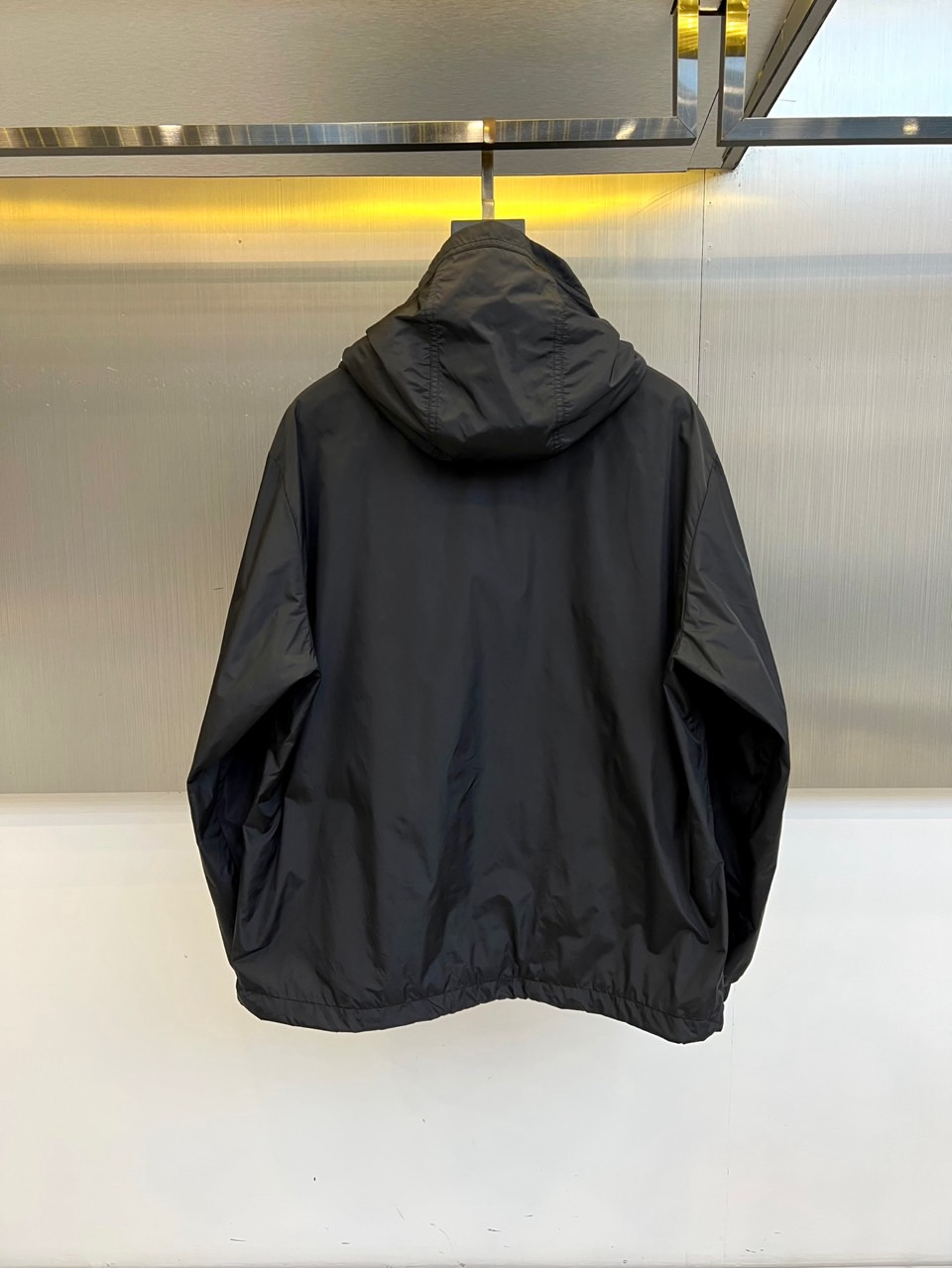 Mon蒙口、25s秋冬新品连帽夹克。冷调纯白如阿尔卑斯新雪，金属背景的钨丝灯光为衣身镀上暖金。拉开拉链乍