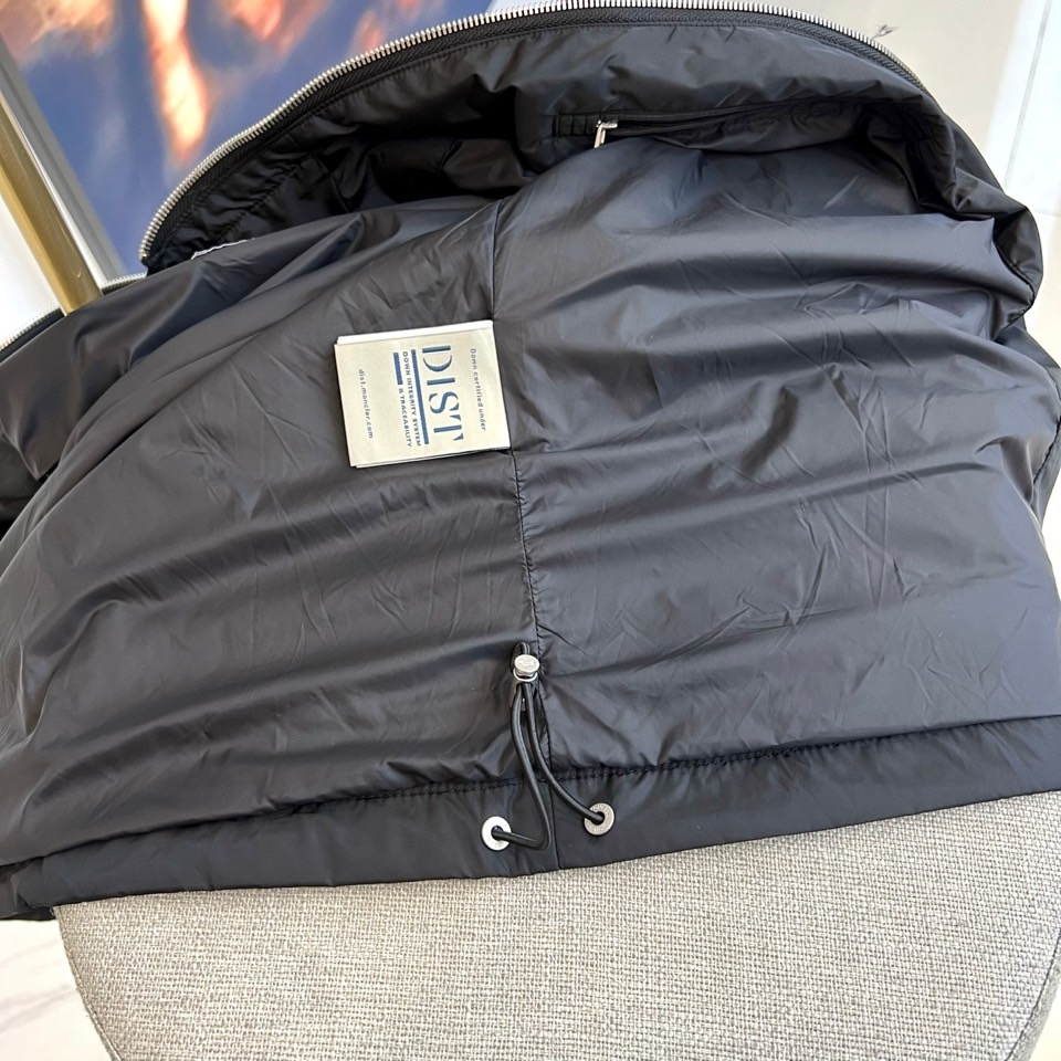 Mon蒙口、25s秋冬新品连帽夹克。冷调纯白如阿尔卑斯新雪，金属背景的钨丝灯光为衣身镀上暖金。拉开拉链乍