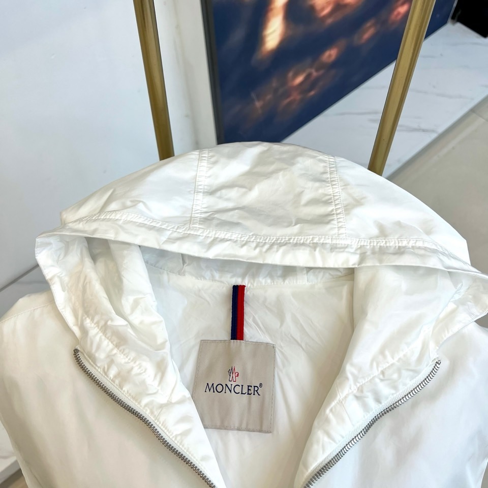 Mon蒙口、25s秋冬新品连帽夹克。冷调纯白如阿尔卑斯新雪，金属背景的钨丝灯光为衣身镀上暖金。拉开拉链乍