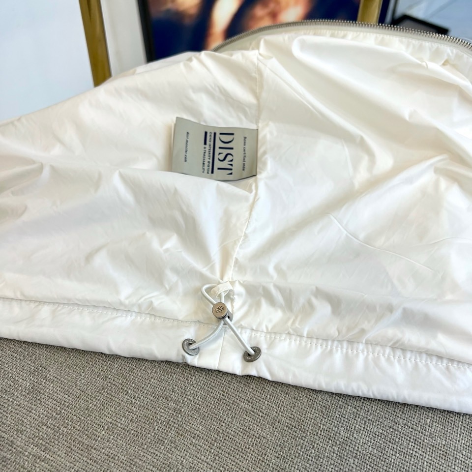 Mon蒙口、25s秋冬新品连帽夹克。冷调纯白如阿尔卑斯新雪，金属背景的钨丝灯光为衣身镀上暖金。拉开拉链乍