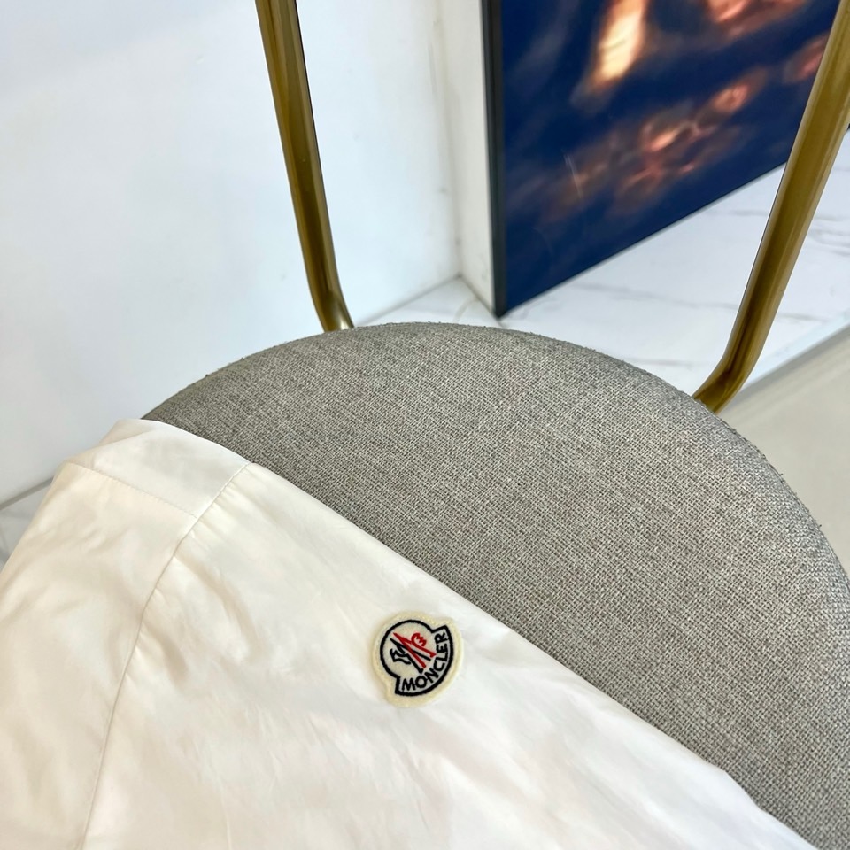 Mon蒙口、25s秋冬新品连帽夹克。冷调纯白如阿尔卑斯新雪，金属背景的钨丝灯光为衣身镀上暖金。拉开拉链乍