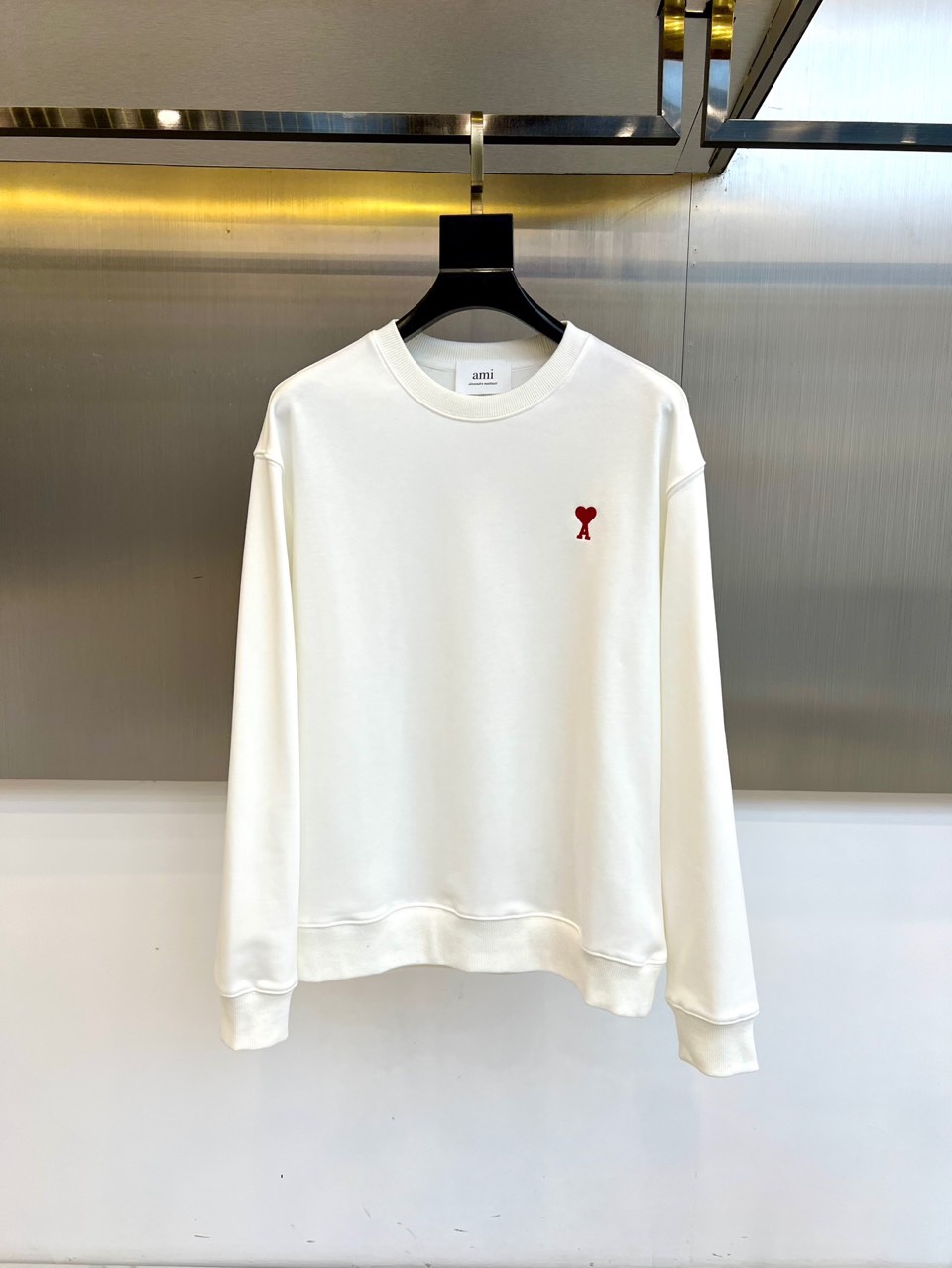 AMI 2025秋冬新品圆领卫衣，以纯净简约的白色为基调，打造秋冬清爽时尚感。胸前点缀品牌标志性红色爱心
