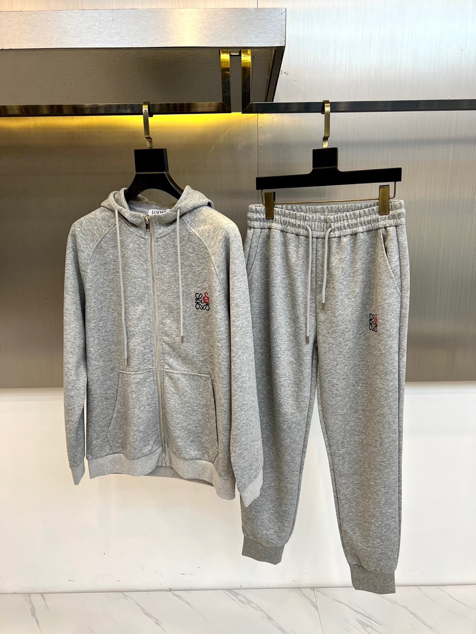 NO:545593,LOEWE and the new gray sports suit in autumn and winter, interpreting the modern and casual aesthetics with simple and high-end gray tone. The suit includes a hooded zipper sweatshirt and the same-colored tying trousers, using high-quality cotton blended fabric to create a soft and skin-friendly wearing experience. The chest of the sweatshirt is decorated with exquisite brand logo embroidery, and the sides of the trousers continue the same design language, highlighting the luxury genes through details. The hooded design is matched with smooth zipper opening and closing, and the tying trousers outlines the neat outline. Its style is perfectly balanced with sports and leisure and high-end fashion, and a loose version  The model ensures freedom of movement, and the gray tone presents a low-key texture. It can be matched with sports shoes to create a full-scene shape, and can also be matched with leather shoes to enhance fashion. This outfit is an ideal choice for both comfort and brand recognition in autumn and winter with exquisite craftsmanship and practical design. M-4XL (model 173, 143 catties upper body L size), loewe, loewe, sneakers, hoodie, sweatshirts, hats, alexander  wang19860909LOEWE罗意威、秋冬新品灰色运动套装,以简约高级的灰调演绎现代休闲美学.套装包含连帽拉链卫衣与同色束脚运动裤,采用高品质棉质混纺面料打造柔软亲肤的穿着体验.卫衣胸前饰以精致品牌标识刺绣,裤装侧边延续相同设计语言,通过细节彰显奢华基因.连帽设计搭配顺滑拉链开合,束脚裤型勾勒利落轮廓.其风格完美平衡运动休闲与高级时尚,宽松版型确保活动自由度,灰色调呈现低调质感.既能搭配运动鞋打造全场景造型,亦可搭配皮革鞋履提升时尚度.这套服装以精湛工艺与实用设计,成为秋冬季节兼具舒适性与品牌辨识度的理想选择.M-4XL（模特173,143斤上身L码）,,loewe,loewe,sneakers,hoodie,sweatshirts,hats,alexander wang,Men's clothing