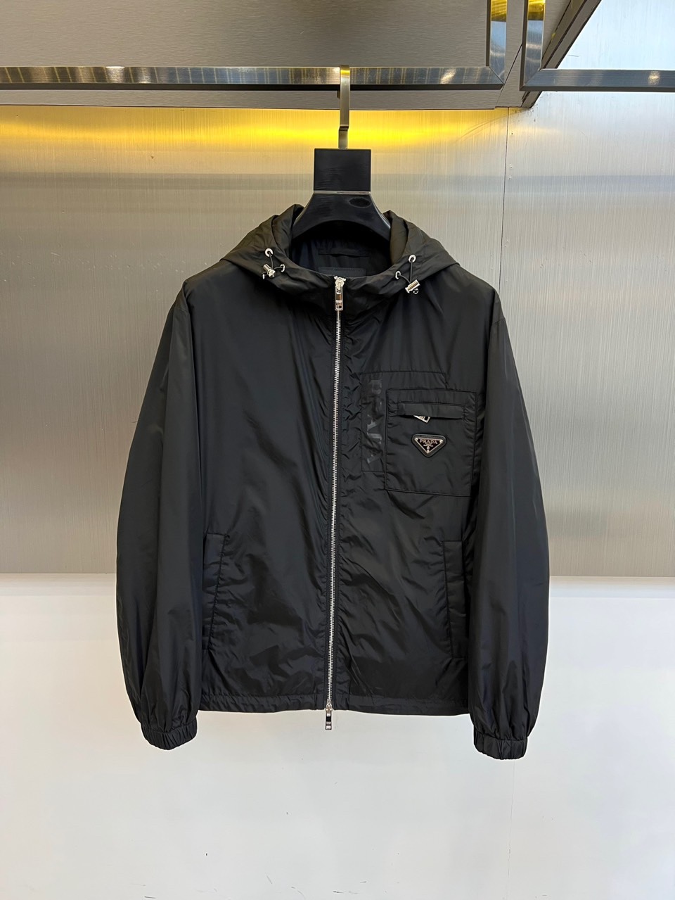 NO:545623,Prad and new black hooded jackets in autumn and winter interpret modern urban aesthetics with minimalist design. They use the brand’s iconic high-tech nylon fabric to create a crisp outline, with the hooded design and smooth zipper opening and closing. The left chest is embellished with a classic triangle enamel logo to enhance the brand recognition with metallic luster. The metal snap decoration and side three-dimensional pockets show exquisite craftsmanship, and the ribbed edge-closing process ensures windproof performance. The style perfectly combines functionalism and Italian exquisiteness, and the black tone demonstrates low-key luxury temperament. It can be matched with casual pants to create a city travel style, and can also be layered for business and casual occasions. This jacket has an iconic detail and pragmatic design, becoming a must-have item for crossing scenes in autumn and winter. 48-56 (model 173, 143 catties upper body 50 yards),, prada, prada, jackets &  coats, jackets & coats,hats,alexander wang19860909Prad普拉、秋冬新品黑色连帽夹克外套,以极简设计诠释现代都市美学.采用品牌标志性的高科技尼龙面料打造挺括轮廓,连帽设计与顺滑拉链开合兼顾实用功能.左胸点缀经典三角形珐琅徽标,以金属光泽提升品牌辨识度.金属按扣装饰与侧边立体口袋展现精湛工艺,罗纹收边工艺确保防风性能.其风格完美融合机能主义与意式精致,黑色基调彰显低调奢华气质.既能搭配休闲裤打造城市出行造型,亦可层叠穿搭应对商务休闲场合.这件夹克以标志性细节与实用主义设计,成为秋冬季节跨越场景的必备单品.48-56（模特173,143斤上身50码）,,prada,prada,jackets & coats,jackets & coats,hats,alexander wang,Men's clothing