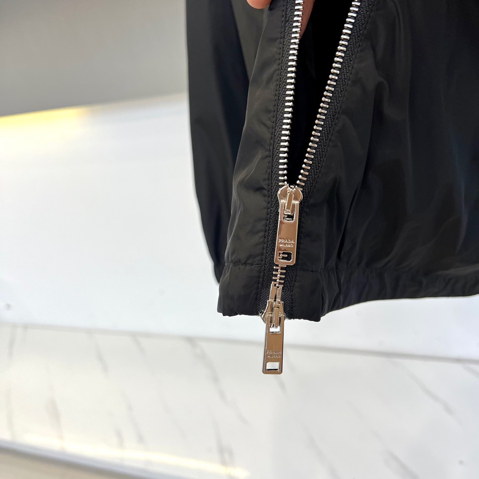 Prad普拉、2025秋冬新品黑色连帽夹克外套，以极简设计诠释现代都市美学。采用品牌标志性的高科技尼龙面