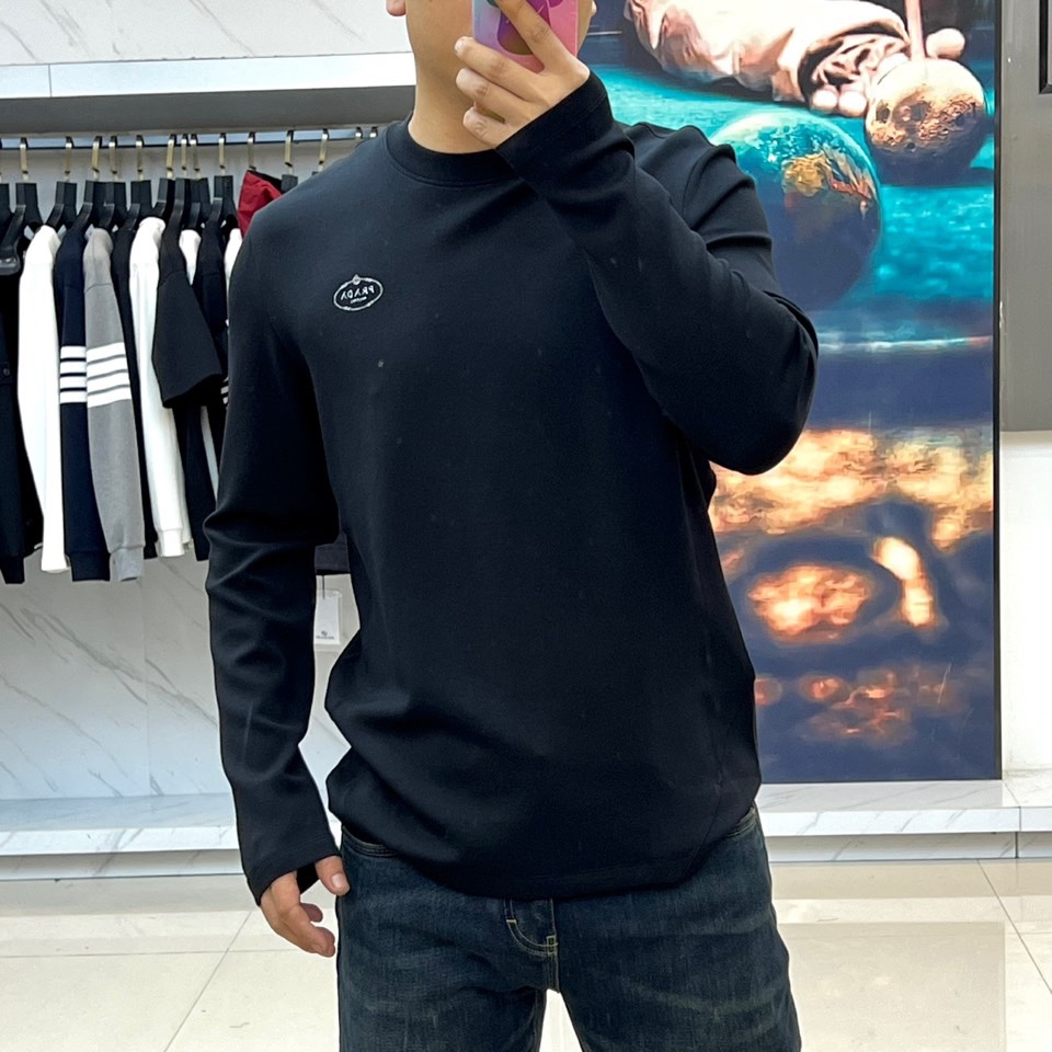 Prad普拉、2025秋冬新品P家简约长袖上衣这款白色长袖上衣采用经典圆领设计与立体剪裁，左胸处装饰品牌