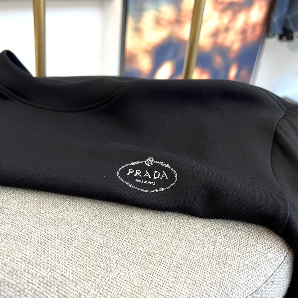 Prad普拉、2025秋冬新品P家简约长袖上衣这款白色长袖上衣采用经典圆领设计与立体剪裁，左胸处装饰品牌