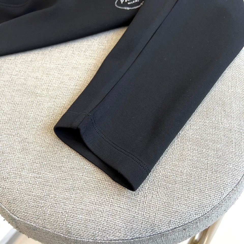 Prad普拉、2025秋冬新品P家简约长袖上衣这款白色长袖上衣采用经典圆领设计与立体剪裁，左胸处装饰品牌