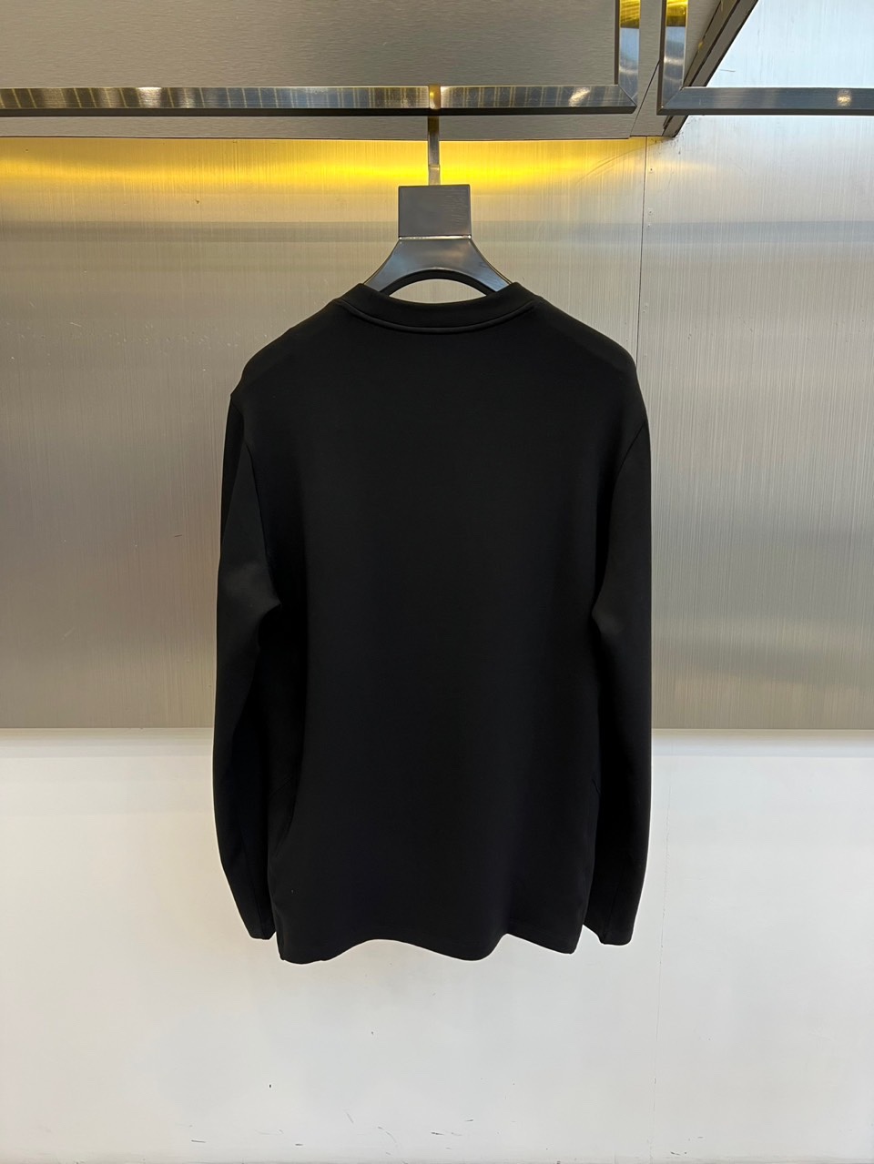 Prad普拉、2025秋冬新品P家简约长袖上衣这款白色长袖上衣采用经典圆领设计与立体剪裁，左胸处装饰品牌