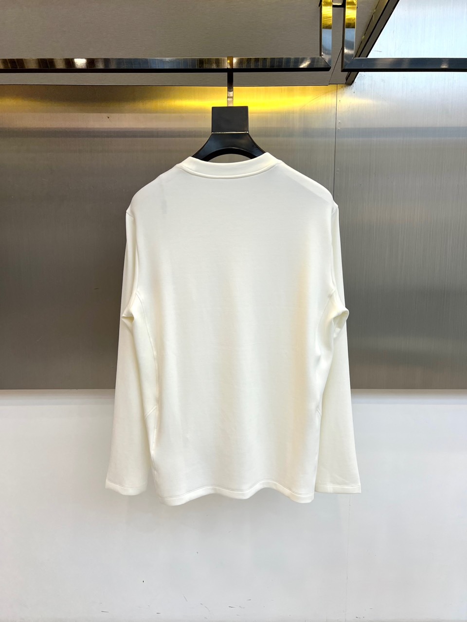 Prad普拉、2025秋冬新品P家简约长袖上衣这款白色长袖上衣采用经典圆领设计与立体剪裁，左胸处装饰品牌