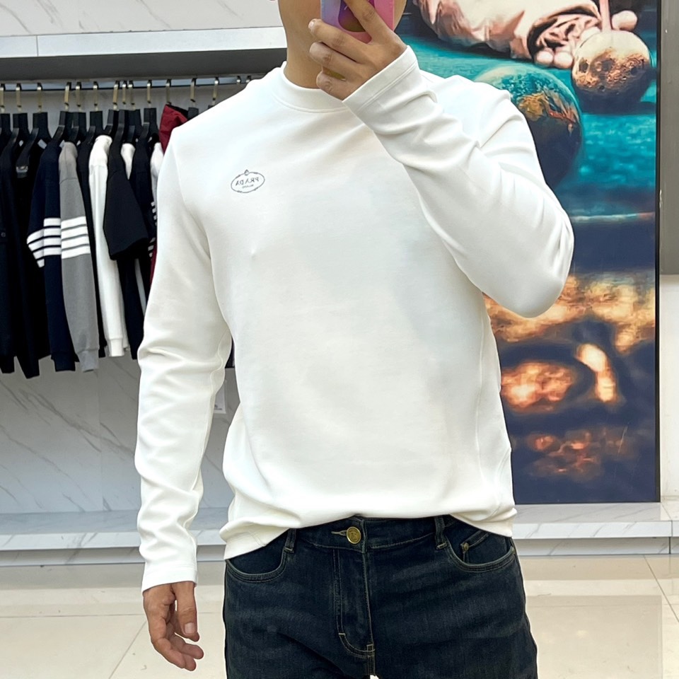 Prad普拉、2025秋冬新品P家简约长袖上衣这款白色长袖上衣采用经典圆领设计与立体剪裁，左胸处装饰品牌