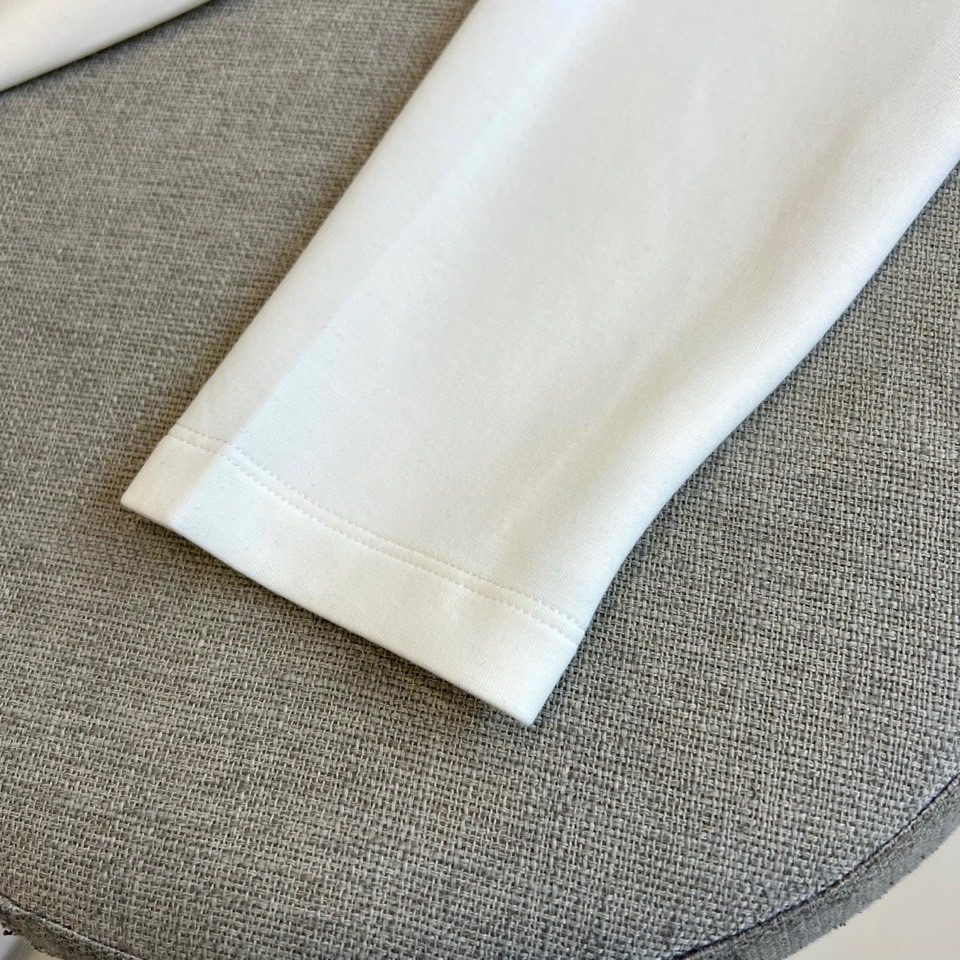 Prad普拉、2025秋冬新品P家简约长袖上衣这款白色长袖上衣采用经典圆领设计与立体剪裁，左胸处装饰品牌