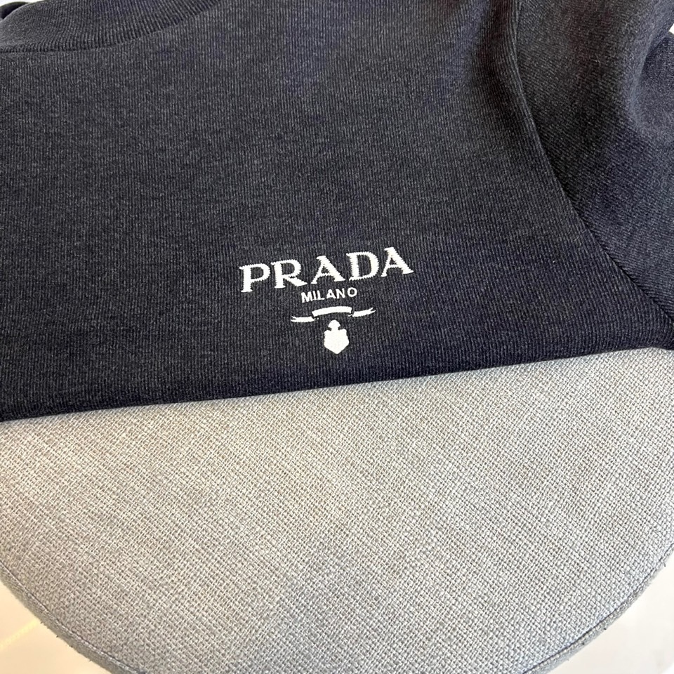 Prad普拉、2025秋冬新品 P家标志长袖T恤。这款白色长袖上衣采用简约半高领设计,左胸处饰有品牌经典