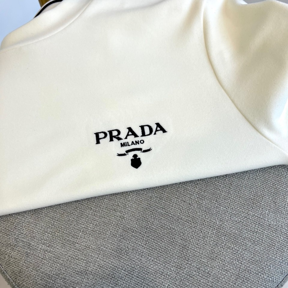 Prad普拉、2025秋冬新品 P家标志长袖T恤。这款白色长袖上衣采用简约半高领设计,左胸处饰有品牌经典