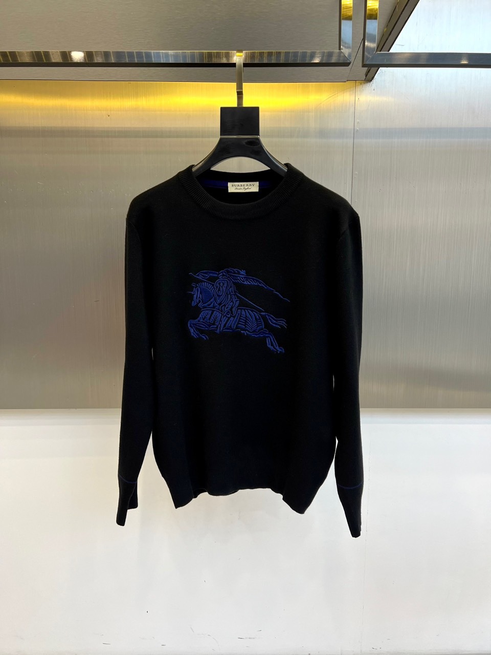 NO:564089,Burberry, new autumn and winter products   Burberry Collection Knight Logo Sweater, this white round-neck sweater is woven from worsted cotton yarn, and the surface of the fabric presents a delicate texture. The jacquard craftsmanship in the center of the front accurately restores the brand's iconic Knight logo, and dark blue silk thread outlines the classic image of riding a horse and holding a flag.  The pattern and cuffs are embellished with ribbed edges of the same color. The logo is inherited from the knight totem from the brand archives in 1901, which symbolizes the spirit of British aristocracy. The version adopts a moderately loose silhouette design, which not only ensures wearing comfort but also maintains neat lines. The pure white background highlights the  The exquisite craftsmanship of the jacquard pattern and the cotton material bring a skin-friendly and breathable wearing experience. It can be paired with casual pants to show simple elegance, or with a skirt to create a college style. Through the combination of the iconic logo and natural materials, Burberry's aesthetic concept of integrating century-old heritage with modern wearability is interpreted. 48-56 (model 173, 143 pounds, upper body size 50),, burberry, burberry, skirts, sweaters, alexander   wang19860909Bur巴宝莉、秋冬新品 巴宝莉典藏骑士徽标毛衣,这款白色圆领毛衣采用精纺棉纱织造,面料表面呈现细腻的肌理感.正面中央以提花工艺精准还原品牌标志性骑士徽标,深蓝色丝线勾勒出骑马执旗的经典图案,袖口点缀同色系罗纹收边.徽标传承自1901年品牌档案库的骑士图腾,象征英伦贵族精神.版型采用适度宽松的廓形设计,既保证穿着舒适度又保持利落线条.纯白底色凸显提花图案的精湛工艺,棉质材质带来亲肤透气的穿着体验.既可搭配休闲裤展现简约优雅,也可搭配半身裙打造学院风格.通过标志性徽标与天然材质的结合,诠释巴宝莉将百年传承与现代实穿性相融合的美学理念.48-56（模特173,143斤上身50码）,,burberry,burberry,skirts,sweaters,alexander wang,Men's clothing