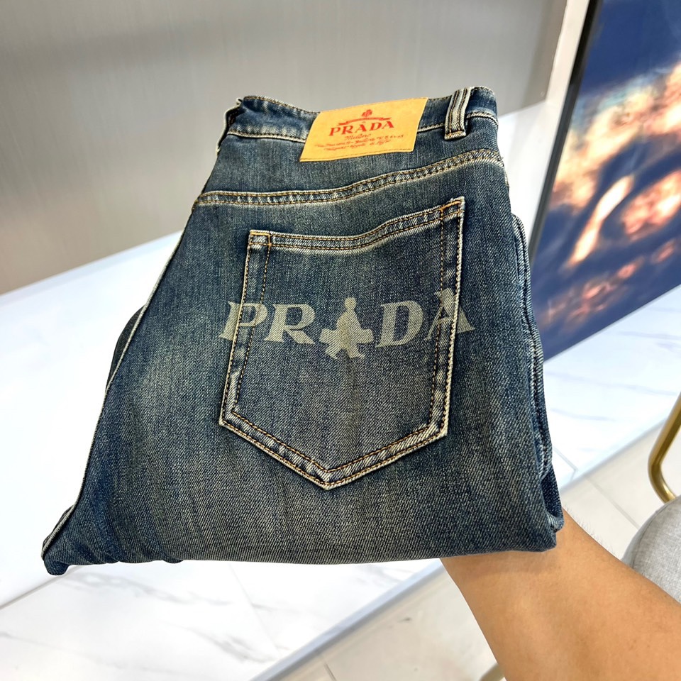 PRADA普拉、2025秋冬新品深蓝色牛仔裤，采用水洗工艺打造自然磨损与褪色效果，呈现复古质感。宽松版型