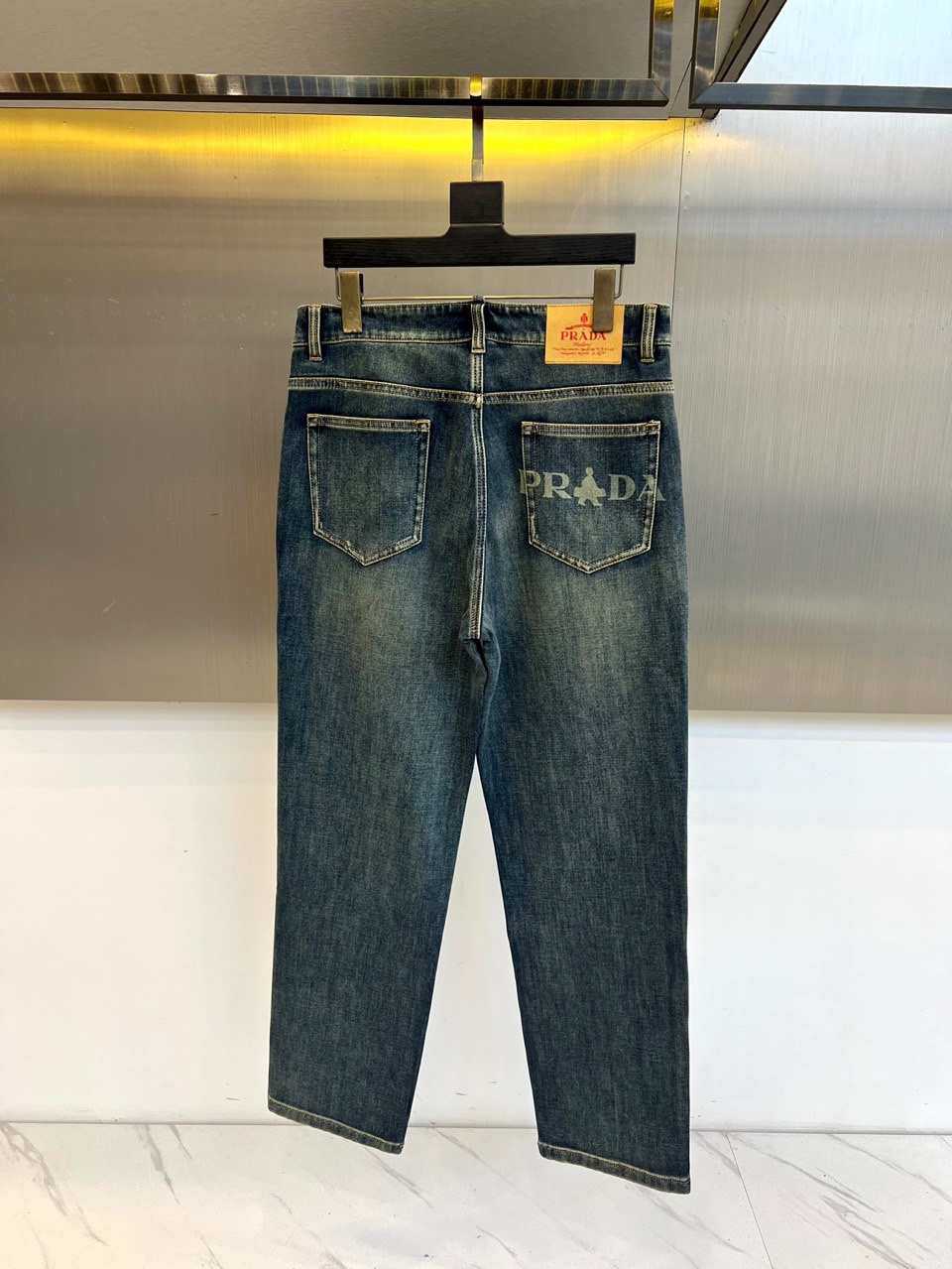 PRADA普拉、2025秋冬新品深蓝色牛仔裤，采用水洗工艺打造自然磨损与褪色效果，呈现复古质感。宽松版型