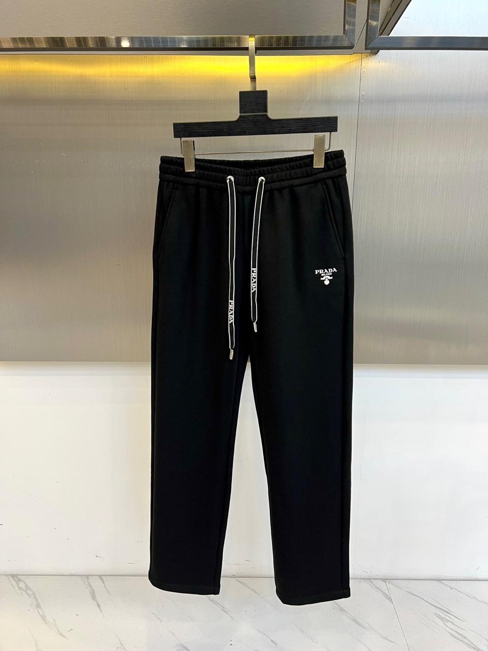 Prad普拉、2025秋冬新品风格男士休闲裤，这款黑色休闲裤采用PRADA标志性设计，左腿外侧饰有白色品