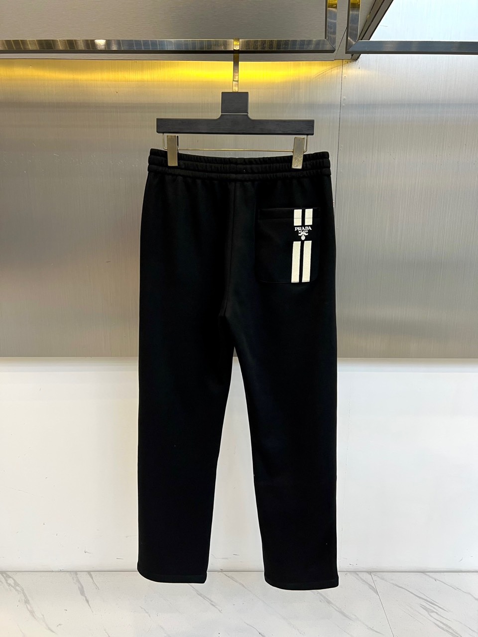 Prad普拉、2025秋冬新品风格男士休闲裤，这款黑色休闲裤采用PRADA标志性设计，左腿外侧饰有白色品