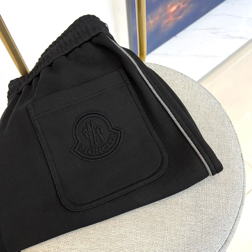 Mon蒙口、2025秋冬新品风格运动休闲裤。这款运动裤采用蒙口标志性设计，裤身两侧饰有浅灰色条纹，左侧裤