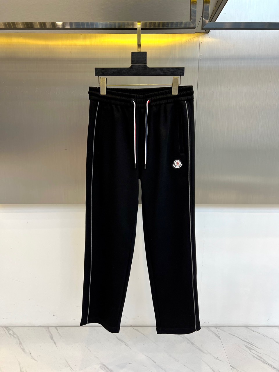 Mon蒙口、2025秋冬新品风格运动休闲裤。这款运动裤采用蒙口标志性设计，裤身两侧饰有浅灰色条纹，左侧裤