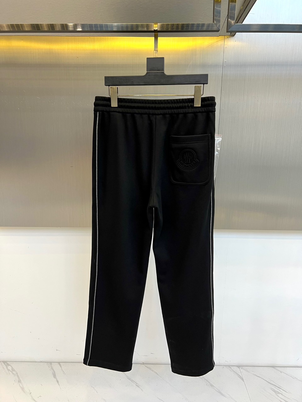 Mon蒙口、2025秋冬新品风格运动休闲裤。这款运动裤采用蒙口标志性设计，裤身两侧饰有浅灰色条纹，左侧裤