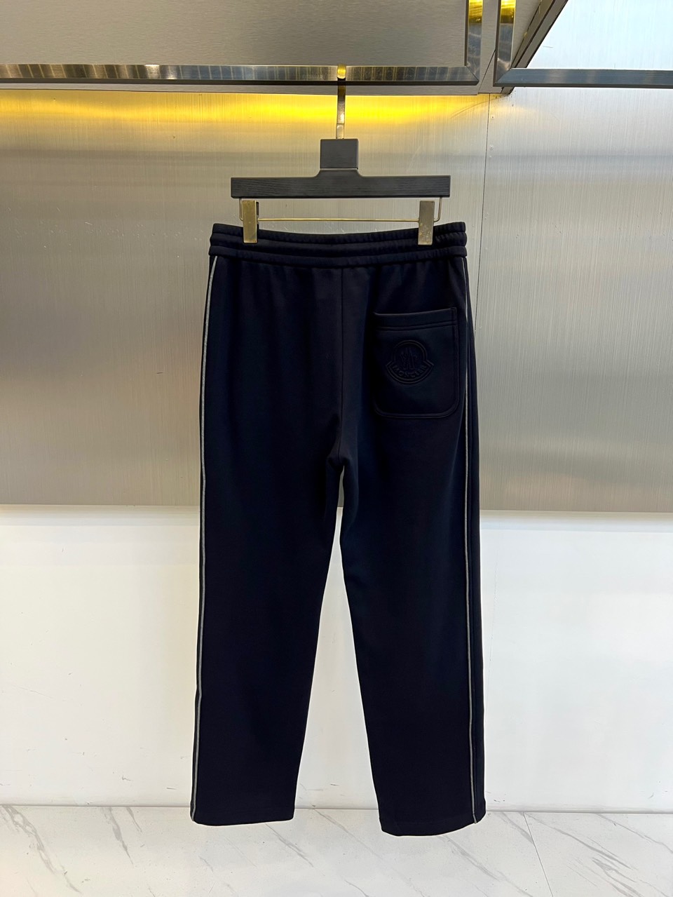 Mon蒙口、2025秋冬新品风格运动休闲裤。这款运动裤采用蒙口标志性设计，裤身两侧饰有浅灰色条纹，左侧裤