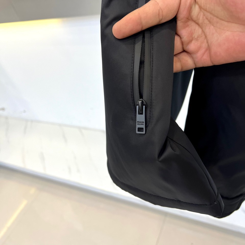 Prad普拉、2025秋冬新品 PRADA科技防护羽绒服。深蓝色连帽设计搭配精密拉链系统，左胸红色织带镶