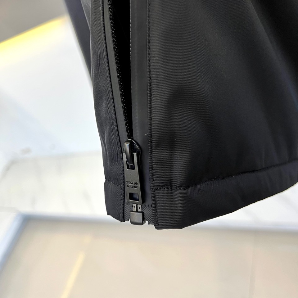 Prad普拉、2025秋冬新品 PRADA科技防护羽绒服。深蓝色连帽设计搭配精密拉链系统，左胸红色织带镶