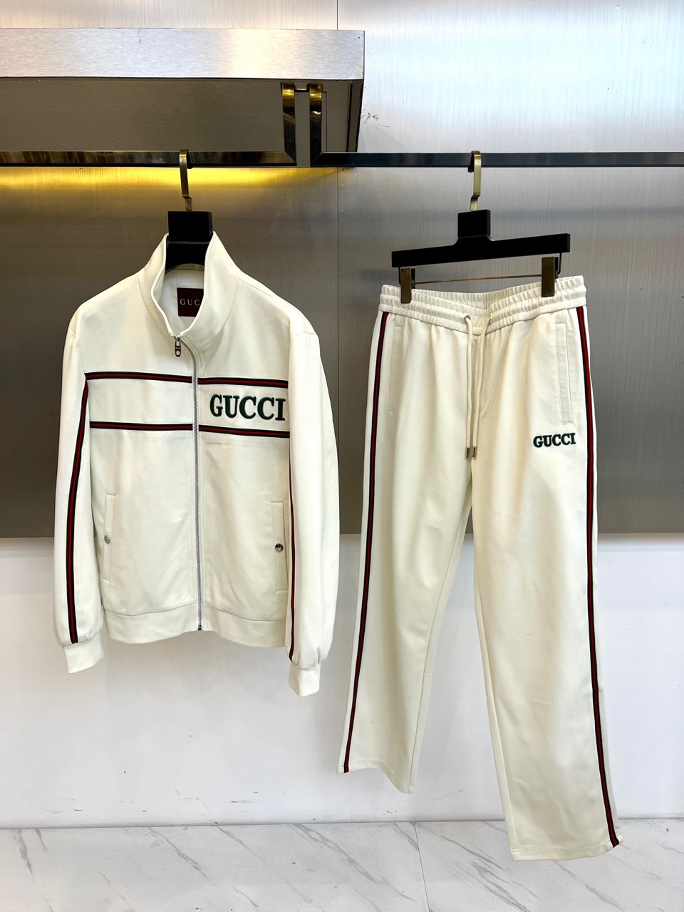 NO:601538,Gucci, the new autumn and winter 2025 suit, interprets modern luxury sports style in all white tones. The suit includes a stand-up collar zipper jacket and a pair of casual trousers of the same color, with a pure and neat overall shape. The classic red and green webbing on the chest of the jacket echoes the stripes on the sleeve side, and is paired with the eye-catching GUCCI letter logo, which instantly enhances brand recognition. The trousers are cut in a loose and comfortable style, and are also decorated with red and green stripes on the sides, forming a clever connection with the top, and the waist  The drawstring design takes into account both leisure and practical functions. This series cleverly combines brand genes and sports aesthetics, and exquisite craftsmanship and high-quality fabrics ensure the wearing experience and high-end texture. Whether it is daily casual or fashionable occasions, this outfit can easily create a modern style that is both energetic and elegant, showing an eclectic fashion attitude. 48-56 (model 173, 143 pounds, upper body size 50),, gucci, gucci, jackets  & coats,alexander wang19860909Gucc古驰、2025秋冬新品套装,以全白色调演绎现代奢华运动风尚.套装包含一件立领拉链外套和一条同色系休闲长裤,整体造型纯净利落.外套胸前的经典红绿织带与袖侧条纹相呼应,搭配醒目的GUCCI字母标识,瞬间提升品牌辨识度.裤装采用宽松舒适的剪裁,侧边同样饰以红绿条纹,与上衣形成巧妙衔接,腰部抽绳设计兼顾休闲感与实用功能.本系列巧妙融合品牌基因与运动美学,精湛工艺与优质面料确保穿着体验与高级质感.无论是日常休闲还是时尚场合,这套装扮都能轻松营造出兼具活力与优雅的摩登型格,展现不拘一格的时尚态度.48-56（模特173,143斤上身50码）,,gucci,gucci,jackets & coats,alexander wang,Men's clothing