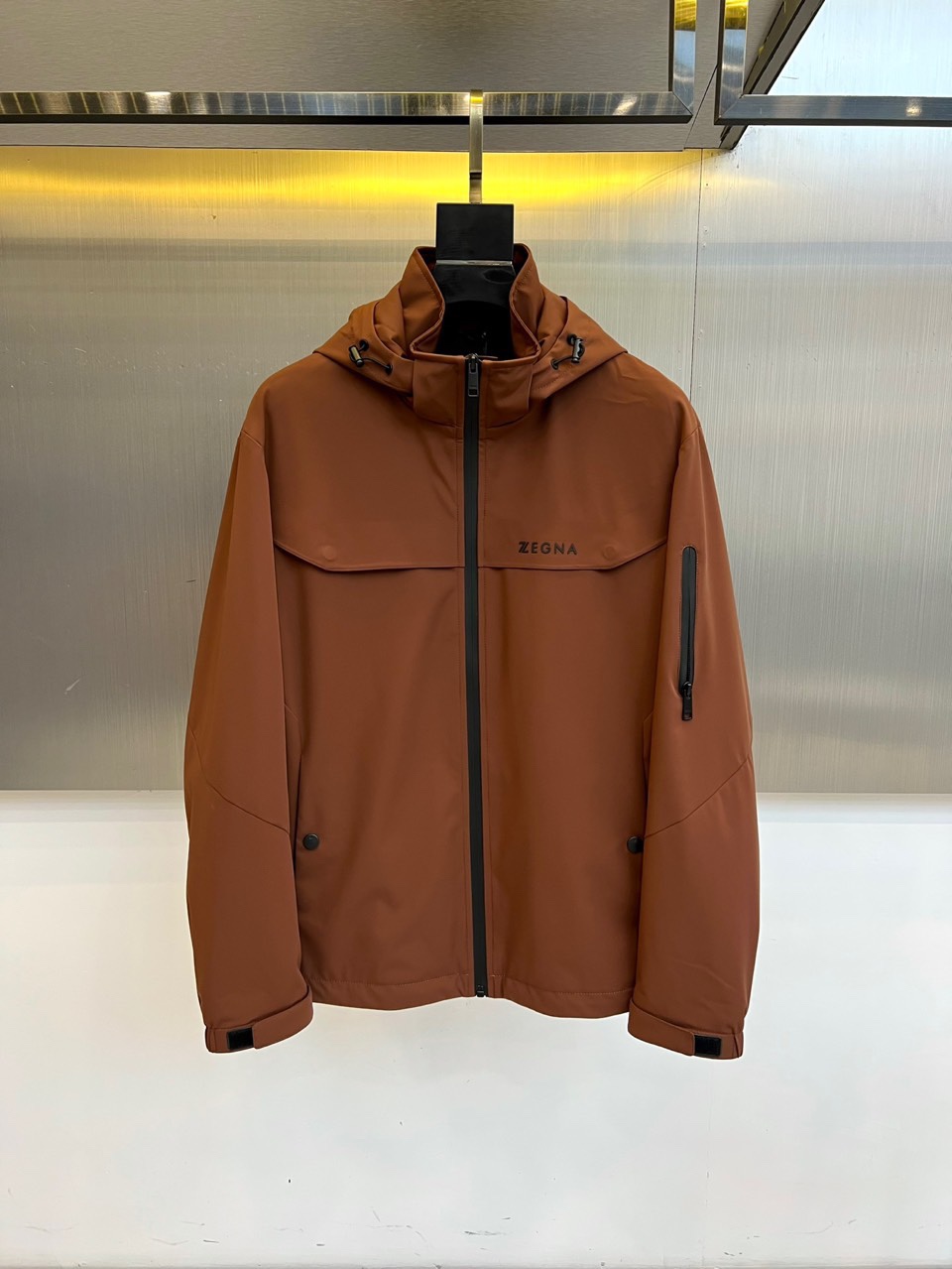 NO:601540,Zegna, the new men's thin cotton windbreaker jacket for autumn and winter 2025, interprets modern urban style with a hooded silhouette with great outdoor functions. The calm brown tone gives the overall simple and elegant visual experience. The body is made of technical polyester fiber fabric, which is crisp and stylish and has excellent windproof protection performance, perfect for autumn and winter weather. The black zipper on the front is smooth and neat, and the practical pockets on the left chest and left arm are designed with ingenuity to meet daily storage needs.  Demand. The shoulders are neatly cut, and the cuffs are equipped with adjustable buckles, demonstrating the brand's precise control of details. The 'ZEGNA' logo on the left chest low-key declares its luxurious pedigree. This jacket perfectly combines outdoor functionality with Italian exquisite aesthetics. Whether walking in the mountains or traveling in the city, it can show a calm and extraordinary gentleman style. 48-56 (model 173, 143 pounds, upper body size 50),,zegna,jackets  & coats,hats,alexander wang19860909Zegna杰尼亚、2025秋冬新品男士薄棉风衣外套,以极具户外机能的连帽廓形演绎现代都市风尚.沉稳的棕色调赋予整体简约大气的视觉感受.衣身采用科技聚酯纤维面料,挺括有型且具备出色的防风防护性能,完美应对秋冬气候.前襟的黑色拉链顺滑利落,左胸及左臂的实用口袋设计融入巧思,满足日常收纳需求.肩部剪裁利落,袖口配有可调节搭扣,彰显品牌对细节的精准把控.左胸的“ZEGNA”标识低调宣示奢华血统.这款外套将户外功能性与意式精致美学完美结合,无论是山野漫步还是都市穿梭,皆能展现从容不凡的绅士型格.48-56（模特173,143斤上身50码）,,zegna,jackets & coats,hats,alexander wang,Men's clothing