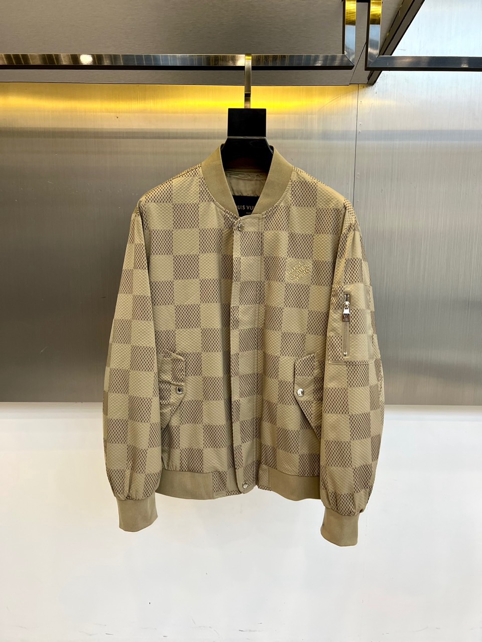 NO:601545,1v Vuitton, a new product for autumn and winter 2025, reshapes the luxury casual style with the classic baseball jacket silhouette. This product is made of khaki checkerboard pattern fabric, which cleverly combines the brand's iconic elements with retro sports style, showing a low-key and restrained luxury texture.  The style details are ingenious. The crisp stand-up collar design outlines a neat silhouette. The front placket is closed with textured buttons. The practical pockets on both sides and the zipper pocket on the left sleeve not only improve functionality, but also add a sense of design layering. The overall cut is smooth, perfectly balancing loose comfort and slim fit.  Its style walks the line between casual and luxurious, with warm khaki colors and timeless checkerboard patterns. Whether paired with simple inner wear or exquisite items, it can instantly enhance the overall style and taste. It can easily handle a variety of occasions from daily outings to high-end social events, showing an extraordinary fashion style. 48-56 (model is 173,143 pounds, upper body size 50),, jackets & coats, alexander wang198609091v威登、2025秋冬新品,以经典棒球夹克廓形重塑奢华休闲风尚.本品精选卡其色棋盘格图案面料,将品牌标志性元素与复古运动风巧妙融合,尽显低调内敛的奢华质感. 款式细节匠心独运挺括的立领设计勾勒利落轮廓,前襟采用质感纽扣开合,两侧实用插袋与左袖的拉链小兜在提升功能性的同时,更添设计层次感.整体剪裁流畅,完美平衡了宽松舒适与修身版型. 其风格游走于休闲与奢华之间,温暖的卡其色系与永恒棋盘格纹,无论是搭配简约内搭或是精致单品,都能即刻提升整体造型品味,轻松驾驭从日常出街到高端社交的多种场合,彰显不凡时尚格调.48-56（模特173,143斤上身50码）,,jackets & coats,alexander wang,Men's clothing