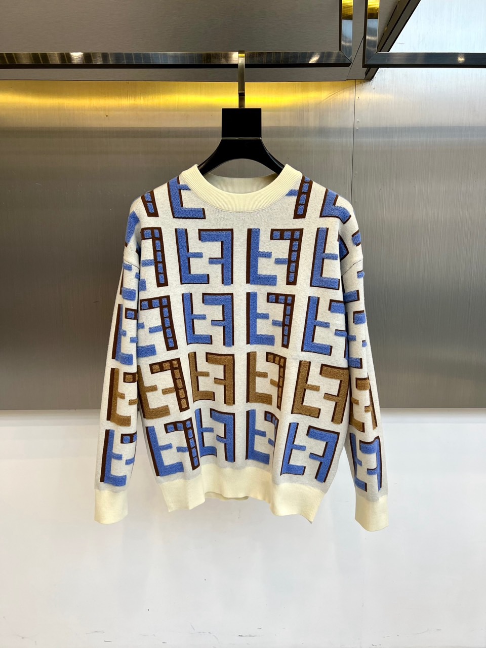 NO:597249,Fend Fendi's new autumn and winter knitted sweaters are based on warm off-white. The brand's classic double F logo is used in a three-dimensional jacquard interpretation of brown and blue gradient yarns, laying out an artistic retro pattern like oil painting strokes. The round neck design is paired with a moderately loose fit.  The shape, cuffs and hem adopt exquisite ribbing technology, which not only ensures the stiffness of the silhouette but also improves the warmth retention performance. The double F pattern is arranged in different proportions to form a patchwork rhythm on the surface of the fabric. The brown color shows a calm texture, and the blue color injects modern vitality. Cotton  The yarn has been treated with a special spindle process to present a delicate and soft texture. This sweater transforms the brand's genes into a wearable artistic symbol. Whether it is paired with retro blue jeans to create a casual style, or it is paired with a leather skirt to create a modern temperament that combines strength and softness, it can become  The key items for autumn and winter layering styles that are both recognizable and practical. 48-56 (model weighs 173,143 pounds, upper body size 50),, fendi, fendi, skirts, jeans, sweaters, alexander  wang19860909Fend芬迪、秋冬新品针织毛衣,以温润米白色为基调,将品牌经典双F标识通过棕色与蓝色的渐变纱线进行立体提花演绎,犹如油画笔触般铺陈出富有艺术感的复古纹样.圆领设计搭配适度宽松的版型,袖口与下摆采用精湛的罗纹收边工艺,既确保廓形挺括度又提升保暖性能.双F图案通过不同比例的缩放排列,在织物表面形成错落有致的韵律感,棕色系呈现沉稳质感,蓝色调注入现代活力.棉质纱线经过特殊纺锤工艺处理,呈现出细腻柔软的肌理触感.这件毛衣将品牌基因转化为可穿戴的艺术符号,无论是搭配复古蓝牛仔裤演绎休闲风尚,还是与皮革半裙碰撞出刚柔并济的摩登气质,都能成为秋冬叠穿造型中兼具辨识度与实穿度的关键单品.48-56（模特173,143斤上身50码）,,fendi,fendi,skirts,jeans,sweaters,alexander wang,Men's clothing