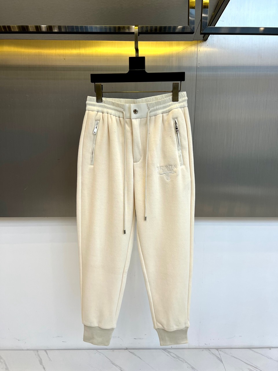 NO:596141,Prad, the new sports casual trousers for autumn and winter 2025, reshape the luxury sports aesthetics with an ankle-shaped silhouette. The style adopts a high-waisted drawstring design, with invisible zipper pockets on both sides and cuff details on the trouser legs. The fabric is marked as cotton, and the lining is velvet-treated to enhance the winter wearing experience. The left leg is decorated with the brand's classic triangle logo embroidery, echoing the brand heritage logo of 'PRADA MILANO DAL 1913'.  Its style combines sports function with fashionable tailoring. The drawstring waistband can be adjusted freely, and the hidden pocket design keeps the lines smooth. The washing label clearly indicates that professional maintenance methods require ironing with a cloth and avoiding natural drying, demonstrating the brand's emphasis on the long-lasting style of the item. The gradient hem and three-dimensional tailoring complement each other, maintaining flexibility of movement without losing the silhouette.  These trousers perfectly combine Italian craftsmanship with street fashion. They can be paired with sweatshirts from the same series to create an overall look, or they can be mixed with coats to show layered aesthetics. From morning yoga to weekend brunch, the velvet lining ensures warmth and comfort, and the triangular logo embroidery low-key highlights the brand's genes. It has become a model for connecting luxury and leisure in the autumn and winter wardrobe. 48-56 (model is 173, 143 pounds, upper body size 50),, brunello  cucinelli,prada,prada,hoodie,sweatshirts,alexander wang19860909Prad普拉、2025秋冬新品运动休闲长裤,以束脚廓形重塑奢华运动美学.款式采用高腰抽绳设计,两侧搭载隐形拉链口袋,裤脚收口细节.面料标注为棉质材质,内里采用加绒处理提升冬季穿着体验.左腿处饰有品牌经典三角徽标刺绣,呼应'PRADA MILANO DAL 1913'的品牌传承标识. 其版型融合运动功能与时尚剪裁,抽绳腰头可自由调节松紧,隐形口袋设计保持线条流畅.洗涤标签明确提示专业养护方式需垫布熨烫并避免自然晾干,彰显品牌对单品持久型格的重视.渐变裤脚与立体剪裁相得益彰,既保持运动灵活性又不失利落轮廓. 这款长裤将意式工艺与街头时尚完美结合,既可搭配同系列卫衣打造整体造型,也能与大衣混搭展现层次美学.从晨间瑜伽到周末brunch,其加绒内里确保保暖舒适,三角徽标刺绣低调彰显品牌基因,成为秋冬衣橱中连接奢华与休闲的典范之作.48-56（模特173,143斤上身50码）,,brunello cucinelli,prada,prada,hoodie,sweatshirts,alexander wang,Men's clothing