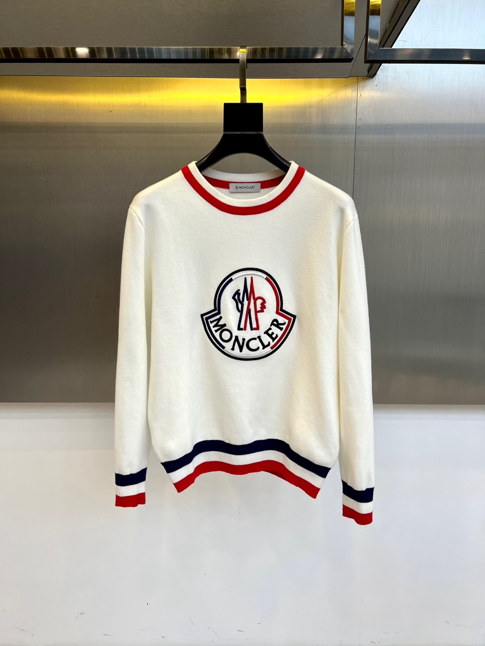 NO:596143,Mon, the 2025 autumn and winter new round-neck sweater, interprets sporty luxury aesthetics with a simple design. The style adopts a classic round-neck silhouette, embellished with the iconic brand logo embroidery on the chest, and the black and red color combinations form a sharp visual contrast with the white base. The cuffs and hem are decorated with red, blue and white striped details, injecting vitality into the simple design. The fabric is made of high-quality cotton to ensure a soft and skin-friendly wearing experience.  Its tailoring pays attention to comfort and freedom of movement, and the ribbing process maintains the stability of the version. It can be paired with casual trousers to create an urban sports style, or it can be combined with denim items for a fun mix and match. From daily outings to weekend leisure, with the clever balance of iconic badges and color details, this sweater has become a carrier that connects high-end craftsmanship and lifestyle, interpreting Moncler's contemporary interpretation of sports aesthetics. 48-56 (model 173, 143 pounds, upper body size 50), Moncler, alexander wang19860909Mon蒙口、2025秋冬新品圆领针织衫,以简约设计诠释运动奢华美学.款式采用经典圆领廓形,胸前点缀标志性品牌徽标刺绣,黑红配色与白色基底形成鲜明视觉对比.袖口及下摆处饰以红蓝白三色条纹细节,为简约设计注入活力韵律.面料选用优质棉质材质,确保柔软亲肤的穿着体验. 其剪裁注重舒适性与活动自由度,罗纹收边工艺保持版型稳定性.可搭配休闲长裤打造都市运动风格,亦可与牛仔单品碰撞出混搭趣味.从日常出街到周末休闲,这款针织衫以标志性徽章与色彩细节的巧妙平衡,成为连接高端工艺与生活方式的载体,诠释Moncler对运动美学的当代解读.48-56（模特173,143斤上身50码）,,Moncler,alexander wang,Men's clothing