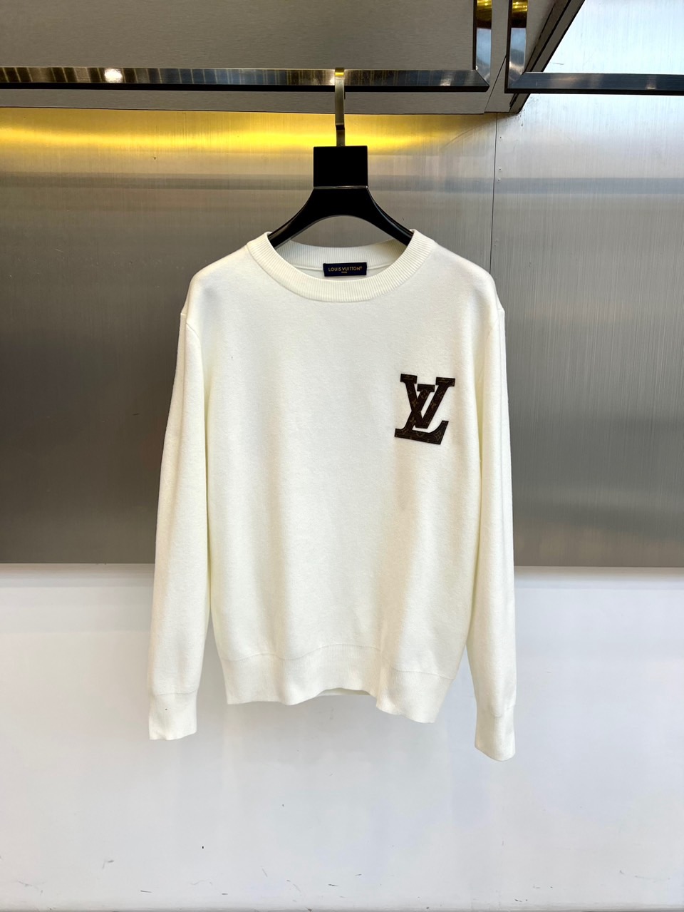 NO:596145,1v Vuitton, the new round-neck knitted sweater for autumn and winter 2025, interprets classic luxury with a simple design. The style adopts a loose round-neck silhouette, and the iconic black 'LV' letter logo is embellished on the left chest, which is in sharp contrast with the pure white fabric. The fabric is strictly made of cotton, and the bilingual label indicates the professional care method. It is recommended to wash the reverse side and iron at low temperature only on the reverse side, highlighting the brand's strict control of quality details.  Its tailoring focuses on daily wearability and creates a comfortable and lazy style through precise silhouette. It can be worn alone with a skirt to show elegance, or layered with a coat to create a layered look. From business meetings to casual gatherings, this sweater, with its exquisite fabric texture and iconic logo design, has become a must-have item that connects the brand's genes with modern lifestyle, interpreting Louis Vuitton's persistent pursuit of quality in daily wear. 48-56 (model is 173, 143 pounds, upper body size 50),, louis  vuitton,louis vuitton,skirts,sweaters,alexander wang198609091v威登、2025秋冬新品圆领针织毛衣,以简约设计诠释经典奢华.款式采用宽松的圆领廓形,左胸点缀标志性黑色'LV'字母标识,与纯净白色面料形成鲜明对比.面料严格选用棉质材质,通过双语标签注明专业护理方式建议反面洗涤并仅限反面低温熨烫,彰显品牌对细节品质的严谨把控. 其剪裁注重日常实穿性,通过精准版型营造舒适慵懒的风格.可单独搭配半裙展现优雅气质,亦可作为内搭与大衣叠穿营造层次感.从商务会面到休闲聚会,这款毛衣以考究的面料质感与标志性标识设计,成为连接品牌基因与现代生活方式的必备单品,诠释路易威登对日常着装品质的执着追求.48-56（模特173,143斤上身50码）,,louis vuitton,louis vuitton,skirts,sweaters,alexander wang,Men's clothing