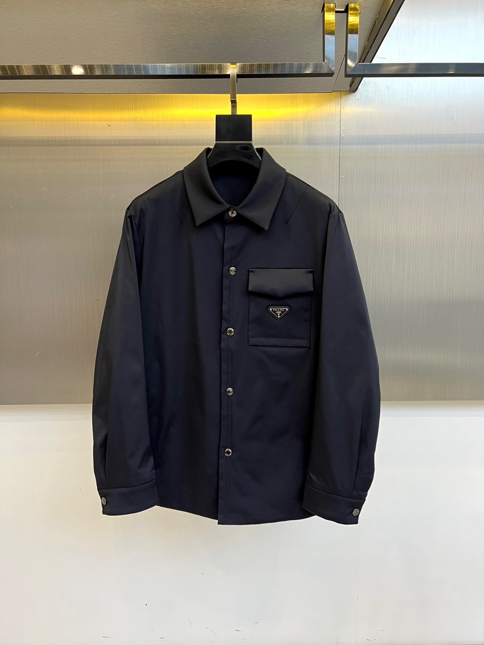 NO:596162,Prad, the new black cotton jacket for autumn and winter 2025, reshapes the winter warm-keeping item with a shirt-style design. It is made of matte black high-tech cotton-feel fabric, which has a light texture and excellent thermal performance. The lapel design continues the brand's neat aesthetics, and the front is equipped with a row of polished metal buttons, which shine with exquisite luster  .There is a body patch pocket on the left chest, and the iconic triangular enamel metal logo is decorated on the top. The classic brand logo is presented in white letters on a black background. The slim fit combines formality and comfort, and the interior is filled with high-quality thermal materials without looking bulky. The style perfectly combines Italian minimalism and pragmatism, with black as the main tone.  It highlights timeless elegance, and the metallic details enhance the luxurious texture. This cotton jacket can be paired with a formal shirt and trousers to create a business casual look, or it can be paired with a turtleneck sweater and casual trousers to show an urban modern style. It is perfectly suitable for office commuting, weekend socializing and other occasions, demonstrating Prada's integration of high-end fashion.  The innovative concept of clothing technology integrated into functional single products provides modern elites who pursue quality life with winter essentials that are both warm and elegant. 48-56 (model weighs 173,143 pounds, upper body size 50),, prada, prada, shirts, alexander  wang19860909Prad普拉、2025秋冬新品黑色棉服,以衬衫式设计重塑冬季保暖单品.采用哑光黑色高科技棉感面料,兼具轻盈质感与卓越保暖性能.翻领设计延续品牌利落美学,前襟配备一排抛光金属纽扣,闪耀精致光泽.左胸设立体贴袋,上方装饰标志性三角形珐琅金属徽标,以黑底白字呈现经典品牌标识.修身剪裁兼顾正式感与舒适度,内里填充优质保暖材料却丝毫不显臃肿.风格上完美融合意式极简主义与实用主义,黑色主调彰显永恒优雅,金属细节提升奢华质感.这款棉服既能搭配正装衬衫与西裤打造商务休闲造型,亦可搭配高领针织衫与休闲长裤展现都市摩登风格,完美适应办公通勤、周末社交等多种场合,诠释Prada将高级时装工艺融入功能性单品的创新理念,为追求品质生活的现代精英提供兼具温度与风度的冬日必备.48-56（模特173,143斤上身50码）,,prada,prada,shirts,alexander wang,Men's clothing