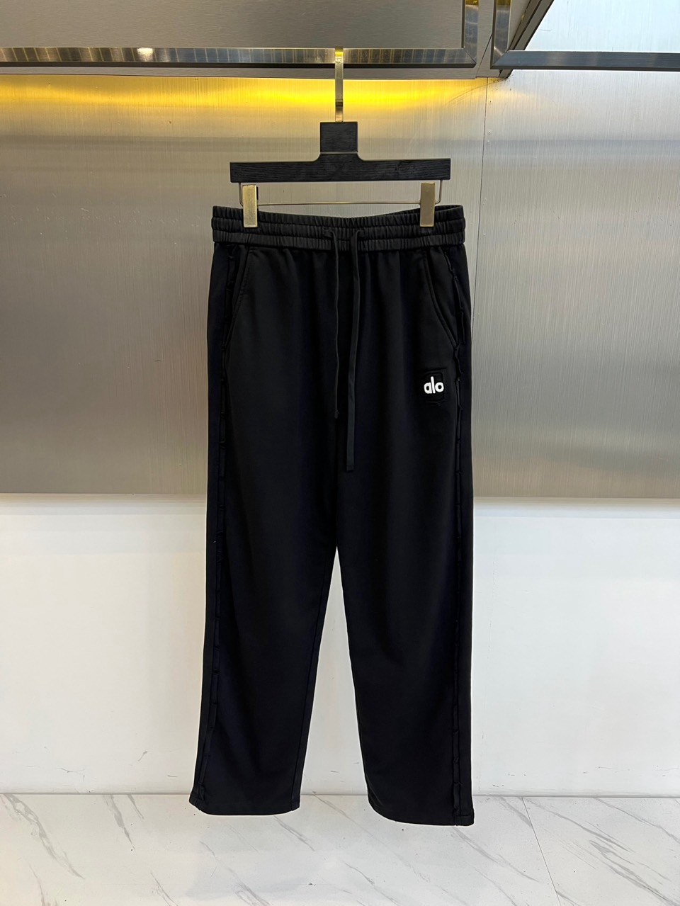 NO:599699,Alo - new sports pants for autumn and winter. The style adopts a straight silhouette with an elastic drawstring waistband. The sides of the pants are decorated with lines extending to the trouser legs. The left leg is embellished with black brand logo embroidery. The fabric is made of innovative technology materials to ensure breathability and freedom of movement when wearing. Its tailoring takes into account daily practical wear and sports needs, and can be paired with a sports vest for strength.  It enhances the overall styling and can also be combined with casual tops to create a mixed and matched level. From the gym to urban street scenes, these trousers use minimalist design language and practical details to become a carrier that connects sports genes and lifestyle, interpreting Alo’s dedicated pursuit of comfortable wearing experience. M-4XL (please state your height and weight when placing an order),,alexander  wang19860909Alo-秋冬新品运动裤,款式采用直筒廓形搭配弹性抽绳腰头,裤身两侧饰有线条装饰延伸至裤脚,左腿处点缀黑色品牌标识刺绣.面料选用创新科技材质,确保穿着时的透气性与活动自由度.其剪裁兼顾日常实穿性与运动需求,可搭配运动背心强化整体造型感,亦能与休闲上衣碰撞出混搭层次.从健身房到城市街景,这款长裤以极简设计语言与实用细节,成为连接运动基因与生活方式的载体,诠释Alo对舒适穿着体验的专注追求.M-4XL（下单请报身高体重）,,alexander wang,Men's clothing