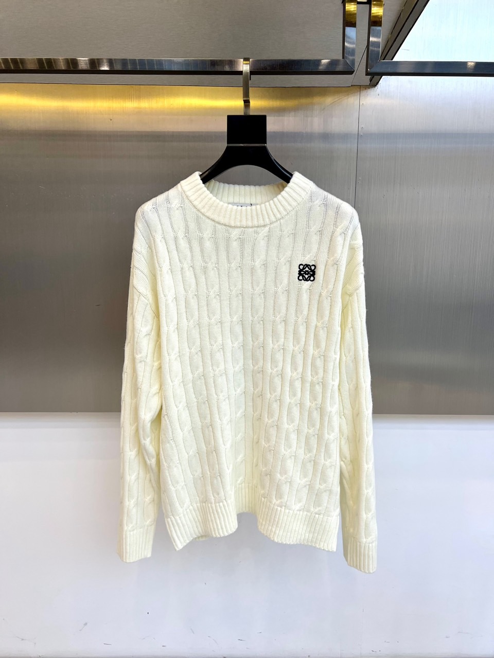 NO:597484,LOEWE's new off-white round neck sweater for autumn and winter 2025 interprets modern elegant aesthetics with exquisite craftsmanship. The style adopts a classic round neck design, and the body is covered with three-dimensional twist knitting texture, which forms rich texture layers through delicate twisting technology. The left chest is embellished with the brand's iconic black Anagram pattern, which uses embroidery technology to present a delicate outline. The fabric is made of high-quality cotton to ensure a soft and skin-friendly wearing experience, and the loose fit combines comfort and fashion.  Its design combines traditional knitting technology with modern aesthetics. The twist texture gives the item a retro feel, and the black Anagram logo low-key highlights the brand's genes. It can be paired with jeans to show casual style, or it can be combined with a skirt to create workplace elegance. From daily outings to business occasions, this sweater has elegant knitting details and a loose silhouette.  It has become a must-have item for autumn and winter that connects exquisite aesthetics and practicality, interpreting LOEWE's continuous exploration of the balance between craftsmanship and design. 48-56 (model weighs 173,143 pounds and is 50 in upper body),,loewe,loewe,skirts,jeans,sweaters,alexander  wang19860909LOEWE罗意威、2025秋冬新品米白色圆领毛衣,以精湛工艺演绎现代优雅美学.款式采用经典圆领设计,衣身满铺立体麻花编织纹理,通过细腻的绞花工艺形成丰富肌理层次.左胸点缀品牌标志性黑色Anagram图案,以刺绣工艺呈现细腻轮廓.面料选用优质棉质材质,确保柔软亲肤的穿着体验,宽松版型兼顾舒适度与时尚感. 其设计将传统针织工艺与现代审美相融合,麻花纹理赋予单品复古气息,黑色Anagram标识低调彰显品牌基因.可搭配牛仔裤展现休闲风尚,亦可与半身裙组合营造职场优雅.从日常出街到商务场合,这款毛衣以考究的编织细节与宽松廓形,成为连接精致美学与实穿主义的秋冬必备单品,诠释LOEWE对工艺与设计平衡的持续探索.48-56（模特173,143斤上身50吗）,,loewe,loewe,skirts,jeans,sweaters,alexander wang,Men's clothing