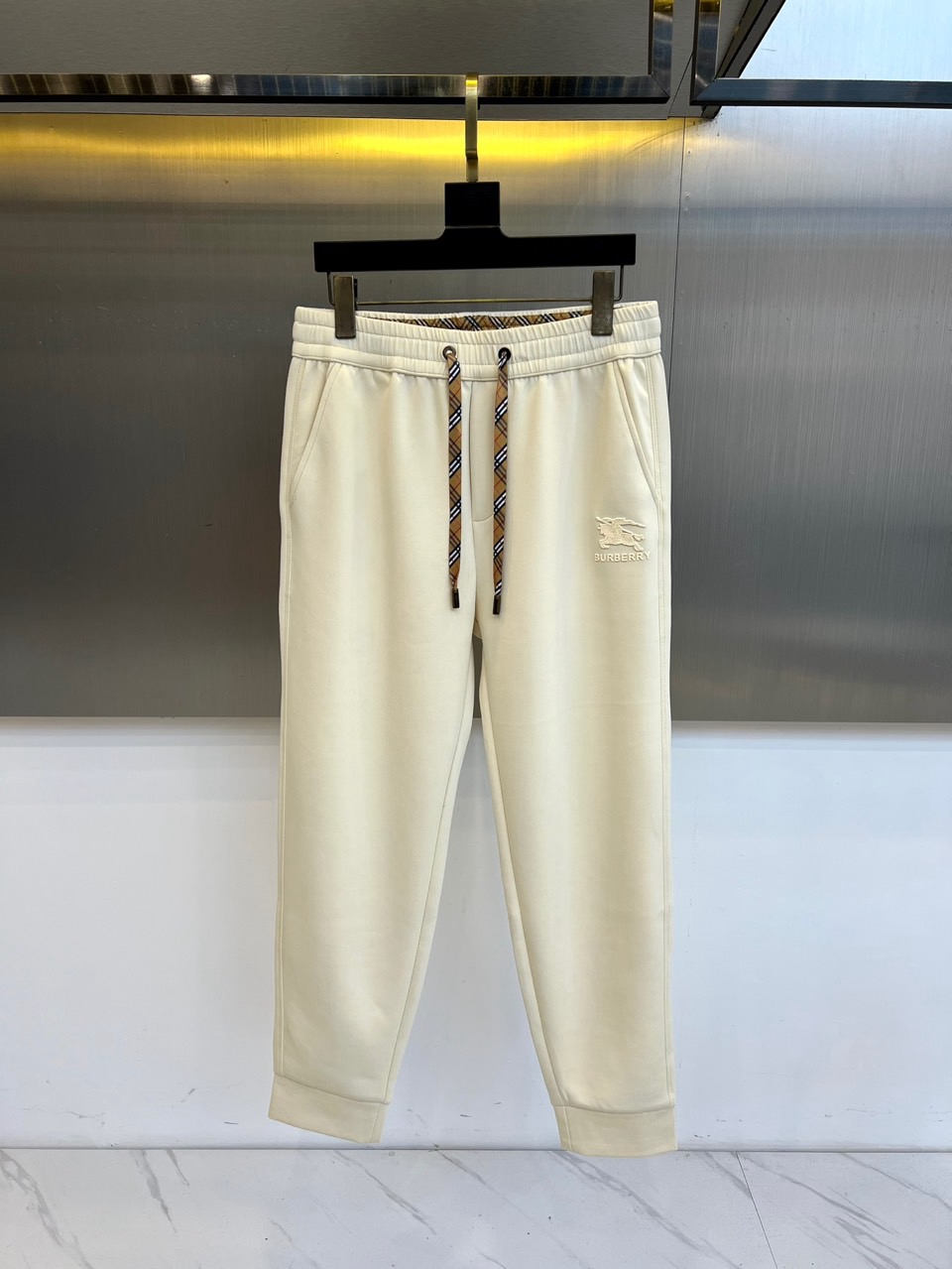 NO:597473,Burberry, 2025 autumn and winter new casual trousers, interpret modern British style with loose tailoring. The style adopts an elastic drawstring waistband design, the waistband is decorated with the brand's classic plaid pattern, and the right trouser leg is embellished with a delicate embroidered logo. The fabric is made of high-tech blended material, containing 88% cotton and 12% elastic fiber, taking into account the skin-friendly feel of cotton and freedom of movement. Its design combines pragmatism and brand heritage, and can be paired with sweaters from the same series to enhance the overall look.  The body feel can also be combined with sports shoes to create a fun mix and match. From urban strolls to casual socializing, these trousers, with the details of plaid drawstrings and embroidered logos, have become a carrier connecting century-old genes and daily wear, interpreting Burberry's contemporary interpretation of elegance and comfort. M-4XL (please state your height and weight when placing an order),, burberry, burberry, sneakers, alexander  wang19860909Bur巴宝莉、2025秋冬新品休闲长裤,以宽松剪裁演绎现代英伦风尚.款式采用弹性抽绳腰头设计,腰头饰有品牌经典格纹图案,右侧裤腿点缀精致刺绣徽标.面料选用高科技混纺材质,含88棉与12弹性纤维,兼顾棉质的亲肤感与活动自由度.其设计将实用主义与品牌传承相融合,可搭配同系列针织衫强化整体感,亦可与运动鞋碰撞出混搭趣味.从都市漫步到休闲社交,这款长裤以格纹抽绳与刺绣徽标的细节巧思,成为连接百年基因与日常着装的载体,诠释Burberry对优雅与舒适并重的当代解读.M-4XL（下单请报身高体重）,,burberry,burberry,sneakers,alexander wang,Men's clothing