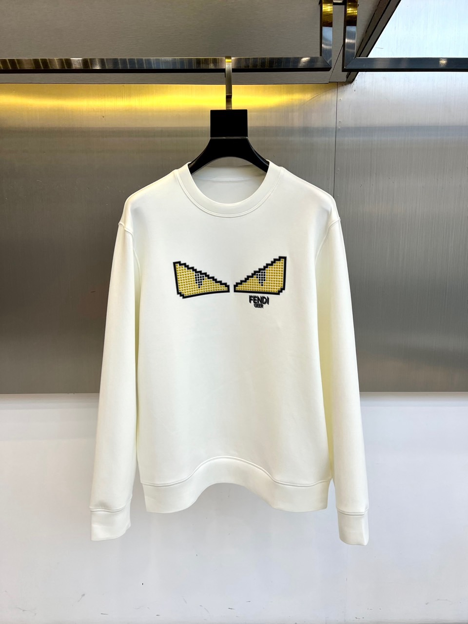 NO:597468,FENDI Fendi's new round-neck sweatshirt for autumn and winter 2025 interprets trendy aesthetics with minimalist design. The style adopts a classic round-neck design, and the collar, cuffs and hem adopt ribbing edge technology to ensure a long-lasting and crisp fit. The front is decorated with the brand's iconic pixel style eyes pattern, in yellow  Color and small black squares intertwine to create a unique visual language, with the black 'FENDI' brand logo embellished below. The fabric is made of a precise ratio of 47 modal, 47 cotton and 6 spandex, which combines the silky drape of modal, the skin-friendly breathability of cotton and the moderate elasticity provided by spandex.  Its design injects digital art genes into daily wear, and the pixel eye pattern shows a youthful trend language. It can be paired with casual trousers to create a street style, or it can be combined with leather items to create a fun mix and match. From daily outings to social occasions, this sweatshirt has innovative pattern design and comfortable fabric experience, becoming a carrier that connects brand genes and contemporary trends.  The washing label clearly guides professional maintenance methods such as low-temperature washing at 30°C and hanging drying, which illustrates FENDI's persistent pursuit of quality details. 50-58 (model weighs 173,143 pounds, upper body size 50),, fendi, fendi, hoodie, sweatshirts, alexander  wang19860909FENDI芬迪、2025秋冬新品圆领卫衣,以极简设计诠释潮流美学.款式采用经典圆领设计,领口、袖口及下摆采用罗纹收边工艺,确保版型持久挺括.正面饰有品牌标志性像素风眼睛图案,黄色与黑色小方块交织出独特视觉语言,下方点缀黑色'FENDI'品牌标识.面料选用47莫代尔、47棉与6氨纶的精密配比,兼具莫代尔的丝滑垂坠感、棉质的亲肤透气性及氨纶提供的适度弹性. 其设计将数码艺术基因注入日常着装,像素眼睛图案展现年轻化潮流语言.可搭配休闲长裤打造街头风格,亦可与皮革单品碰撞出混搭趣味.从日常出街到社交场合,这款卫衣以创新图案设计与舒适面料体验,成为连接品牌基因与当代潮流的载体.洗涤标签明确指导30℃低温洗涤、悬挂晾干等专业养护方式,诠释FENDI对品质细节的执着追求.50-58（模特173,143斤上身50码）,,fendi,fendi,hoodie,sweatshirts,alexander wang,Men's clothing