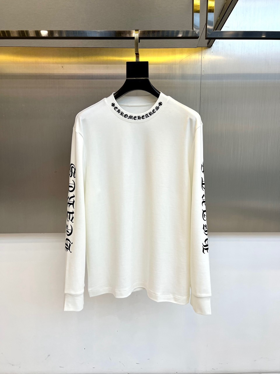 NO:597477,Chrome Hearts  Crow Heart, the new long-sleeved top for autumn and winter 2025, interprets dark luxury aesthetics with minimalist design. The style adopts a classic round neck design, and the neckline is decorated with the brand's iconic black Gothic font logo. The sides of the sleeves are embellished with carefully designed logo combination patterns, which is pure.  The white base is infused with the brand's unique rebellious soul. The fabric is made of a precise ratio of 47 modal, 47 cotton and 6 spandex, which not only maintains the silky drape of modal, but also ensures skin-friendly breathability through cotton, and the spandex component provides just the right elasticity and recovery.  Its design continues the brand's consistent gothic style genes. It can be paired with leather items to enhance the dark temperament, or it can be combined with denim materials to create a mixed and matched level. From daily outings to night socializing, this top has an exquisite fabric ratio and iconic logo design, becoming a link between silver jewelry aesthetics and daily wear.  The carrier of clothing interprets Croxin's in-depth exploration of low-key luxury. The washing label clearly guides professional maintenance methods such as gentle washing at 30 degrees low temperature, hanging drying, etc. to ensure that the clothes are kept in the best condition. 50-58 (model is 173, 143 pounds, upper body size 50),, chrome  hearts,chrome hearts,alexander wang19860909Chrome Hearts 克罗心、2025秋冬新品长袖上衣,以极简设计诠释暗黑奢华美学.款式采用经典圆领设计,领口饰有品牌标志性黑色哥特字体标识,衣袖两侧点缀精心设计的徽标组合图案,为纯净白色基底注入品牌独有的叛逆灵魂.面料选用47莫代尔、47棉与6氨纶的精密配比,既保持莫代尔的丝滑垂坠感,又通过棉质确保亲肤透气性,氨纶成分提供恰到好处的弹性恢复力. 其设计延续品牌一贯的哥特式风格基因,可搭配皮革单品强化暗黑气质,亦可与牛仔材质碰撞出混搭层次.从日常出街到夜间社交,这款上衣以考究的面料配比与标志性标识设计,成为连接银饰美学与日常着装的载体,诠释克罗心对低调奢华的深度探索.洗涤标签明确指导30度低温轻柔洗涤、悬挂晾干等专业养护方式,确保衣物保持最佳状态.50-58（模特173,143斤上身50码）,,chrome hearts,chrome hearts,alexander wang,Men's clothing