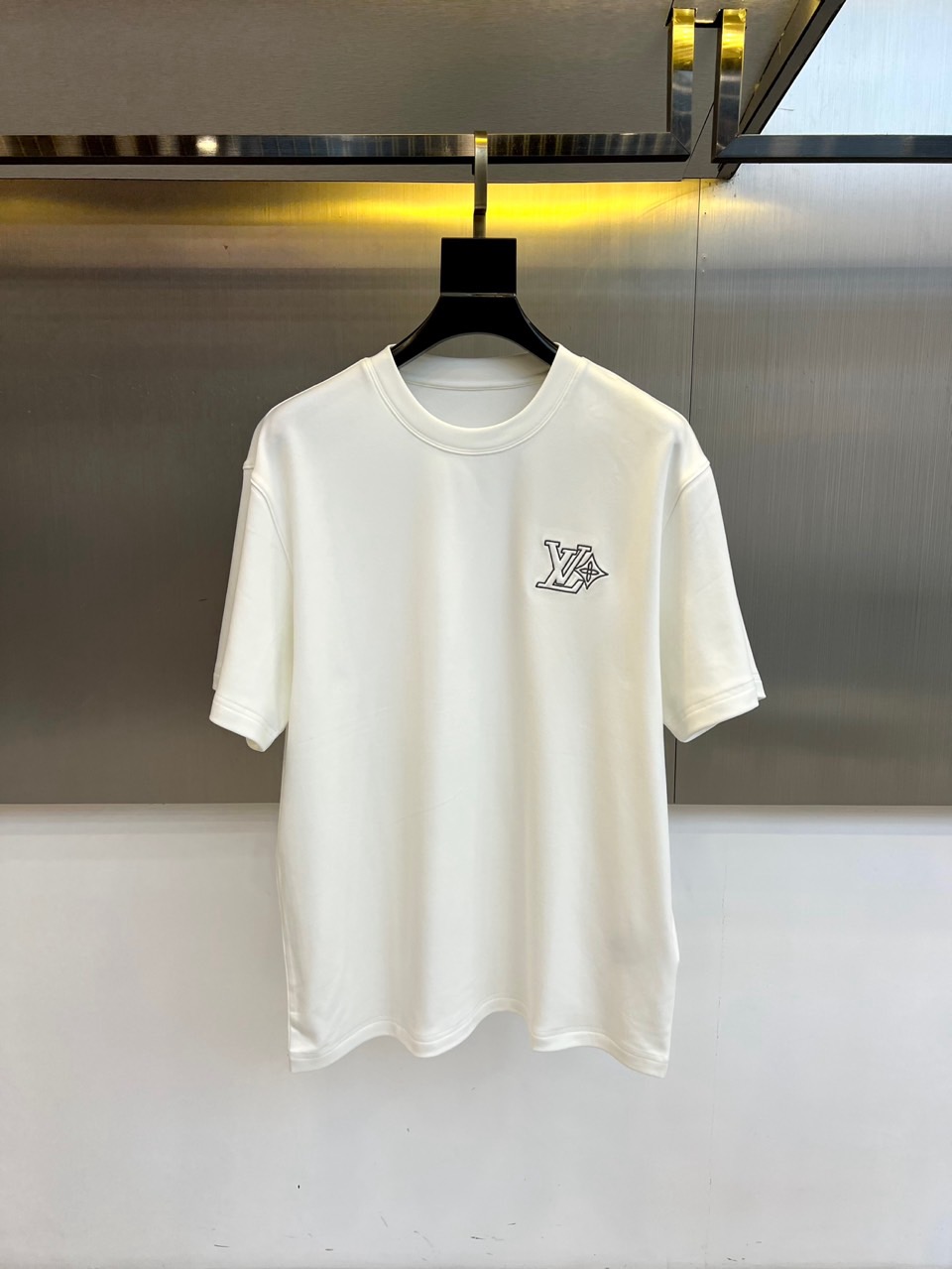 NO:598617,1v Vuitton, 2025 new autumn and winter logo embroidered round neck mid-sleeve T-shirt base layer. This white T-shirt adopts a classic round neck design, with the brand's iconic 'LV' monogram logo exquisitely embroidered on the left chest. The unique arrow element adds modern dynamics to the simple design. The cotton fabric ensures a soft and skin-friendly wearing experience, and the slightly wide version takes into account both comfort and fashionable silhouette. The double-line reinforcement process at the hem ensures durability, and the ribbing at the collar  The white basic model is easy to match and can be worn alone to show a refreshing temperament or as an inner layer to highlight the brand details. The clever combination of arrow elements and letter logos reveals low-key luxury in simplicity, suitable for daily leisure, business leisure and other occasions, and perfectly interprets LV's design concept of integrating classic aesthetics into daily wear. 48-56 (model is 173, 143 pounds, upper body size 50), Louis  vuitton,tees,t-shirt,alexander wang198609091v威登、2025秋冬新品标志刺绣圆领中袖T恤打底衫.这款白色T恤采用经典圆领设计,左胸处精致刺绣着品牌标志性的'LV'字母组合标识,独特的箭头元素为简约设计增添现代动感.棉质面料确保柔软亲肤的穿着体验,微阔版型兼顾舒适性与时尚轮廓.衣摆处的双线加固工艺保证耐久性,领口罗纹处理保持长久不变形.白色基础款易于搭配,既可单穿展现清爽气质,也能作为内搭突显品牌细节.箭头元素与字母标识的巧妙组合,在简约中透露出低调奢华,适合日常休闲、商务休闲等多种场合,完美诠释LV将经典美学融入日常穿着的设计理念.48-56（模特173,143斤上身50码）,,louis vuitton,tees，t-shirt,alexander wang,Men's clothing