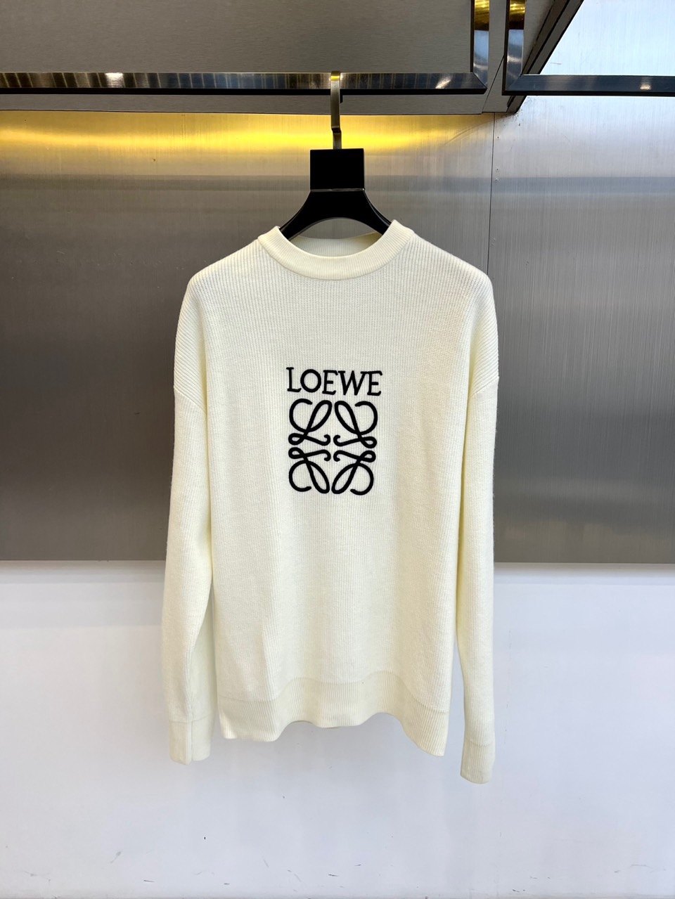 NO:599946,LOEWE, the new off-white crew neck sweater for autumn and winter 2025, interprets Spanish luxury aesthetics with an extremely simple design. The style adopts a classic crew neck silhouette, and the body is made of wool to create a soft texture. The brand's iconic black 'LOEWE' logo and Anagram intertwined pattern are centered on the front. The label clearly indicates the quality of Made in Italy, and strictly abides by international washing standards. Bleaching and tumble drying are prohibited. The reverse side needs to be ironed at low temperature and avoid the printed area.  Its design combines traditional knitting techniques with modern minimalism. The three-dimensional tailoring creates a natural drape. The black logo and off-white background form an elegant contrast. It can be paired with casual trousers to show daily elegance, or it can be combined with suit pants to create a business casual look. From art exhibitions to high-end social occasions, this sweater is made of pure wool.  The inherited genes of skin texture and iconic patterns have become a carrier that connects the brand's century-old craftsmanship with contemporary life, interpreting LOEWE's eternal pursuit of materials and shapes. 48-56 (model weighs 173,143 pounds and has an upper body of 50?),,loewe,loewe,sweaters,business  suit,alexander wang19860909LOEWE罗意威、2025秋冬新品米白色圆领毛衣,以极致简约设计诠释西班牙奢华美学.款式采用经典圆领廓形,衣身采用羊毛材质打造柔软肌理,正面居中呈现品牌标志性黑色'LOEWE'标识与Anagram交织图案.标签明确标注意大利制造品质,严格遵守国际洗涤标准禁止漂白与滚筒烘干,需反面低温熨烫并避开印花部位. 其设计将传统针织工艺与现代极简主义相融合,立体剪裁营造自然垂坠感,黑色标识与米白底色形成优雅对比.可搭配休闲长裤展现日常优雅,亦可与西装裤组合打造商务休闲造型.从艺术展览到高端社交场合,这款毛衣以纯羊毛材质的亲肤质感与标志性图案的传承基因,成为连接品牌百年工艺与当代生活的载体,诠释LOEWE对材质与形制的永恒追求.48-56（模特173,143斤上身50吗）,,loewe,loewe,sweaters,business suit,alexander wang,Men's clothing