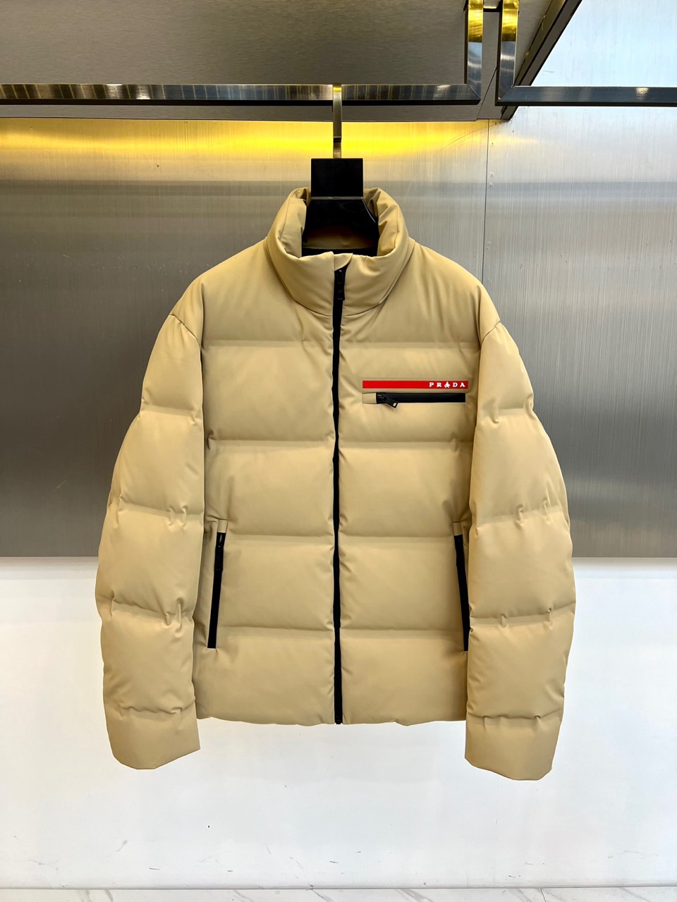 NO:599938,Prad, the new style down jacket for autumn and winter 2025, adopts a neat stand-up collar design and is equipped with a smooth black zipper opening and closing system. The left chest is embellished with the iconic red, white and black three-color webbing, and the white PRADA brand logo is inlaid to highlight the luxury base.  Because the body of the garment is uniformly filled through precise quilting technology, and is equipped with practical pockets with zippers on both sides. The fabric is made of a blend of 87 nylon and 13 spandex, which is both windproof, elastic and wear-resistant; it is filled with high-quality white duck down with 90% down content.  Its design combines high-end fashion genes with pragmatism. It can be paired with formal pants to show a business casual style, or it can be paired with denim items for a fun mix and match. From urban commuting to winter travel, this down jacket has three-dimensional tailoring and professional thermal performance, becoming a link between Italian craftsmanship.  A winter model for daily life. Made in Zhejiang, the precision quality and Class C safety certification interpret PRADA’s dual pursuit of texture and function. 48-56 (model weighs 173,143 pounds, upper body size 50),, prada, prada, down  jacket,alexander wang19860909Prad普拉、2025秋冬新品格调羽绒服,款式采用利落立领设计,搭配顺滑黑色拉链开合系统,左胸点缀标志性红白黑三色织带,镶嵌白色PRADA品牌标识彰显奢华基因.衣身通过精准绗缝工艺确保填充均匀,两侧配备带拉链的实用口袋.面料采用87锦纶与13氨纶混纺材质,兼具防风弹性与耐磨性能；内填充90绒子含量的优质白鸭绒. 其设计将高端时装基因与实用主义相融合,可搭配正装裤展现商务休闲风范,亦可与牛仔单品碰撞出混搭趣味.从都市通勤到冬日旅行,这款羽绒服以立体剪裁与专业保暖性能,成为连接意式工艺与日常生活的冬季典范.浙江制造的精工品质与C类安全认证,诠释PRADA对质感与功能的双重追求.48-56（模特173,143斤上身50码）,,prada,prada,down jacket,alexander wang,Men's clothing